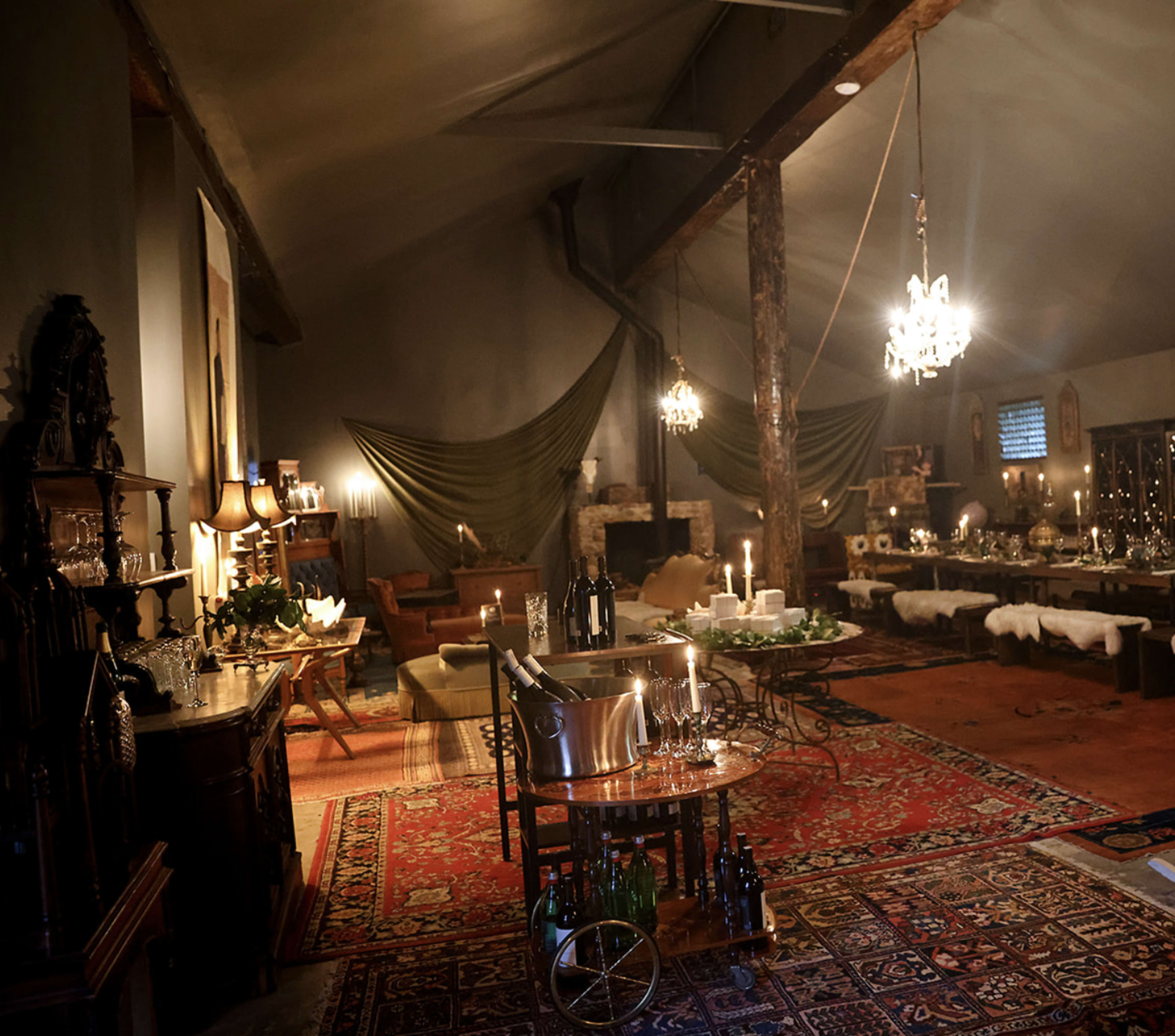 A spacious, dimly lit room with elegant furnishings, a large dining area, and decorative chandeliers hanging from the ceiling.