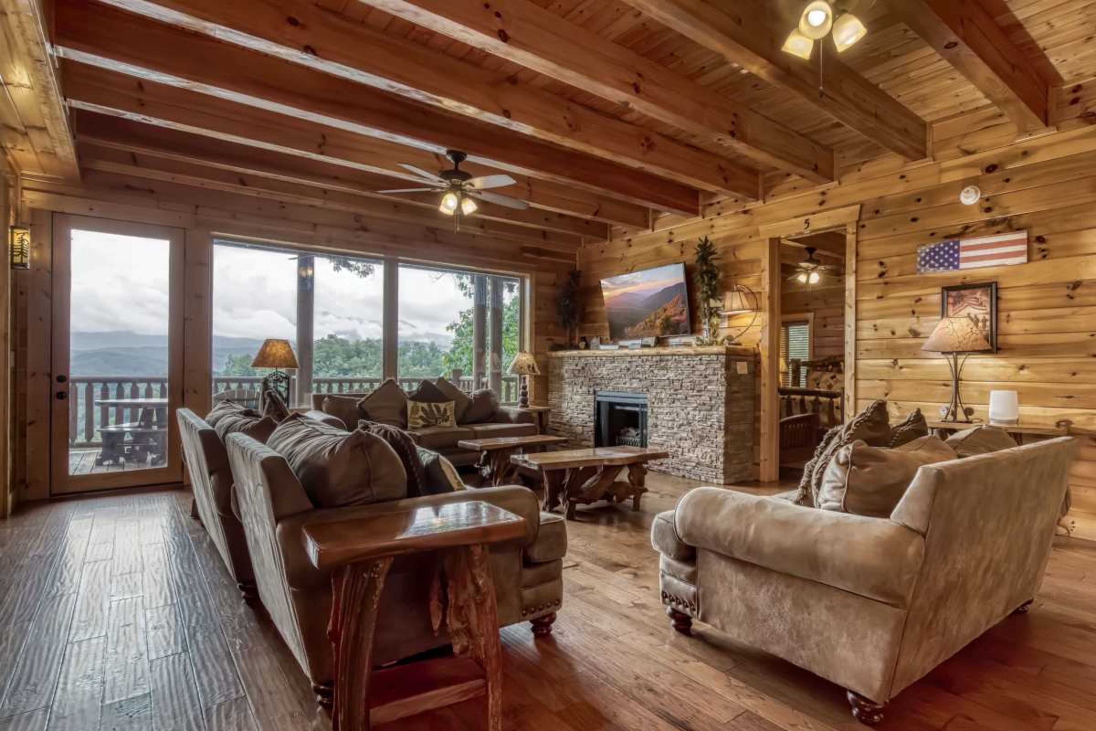 The living room features wooden beams, stone accents, and large windows that open to a scenic view.