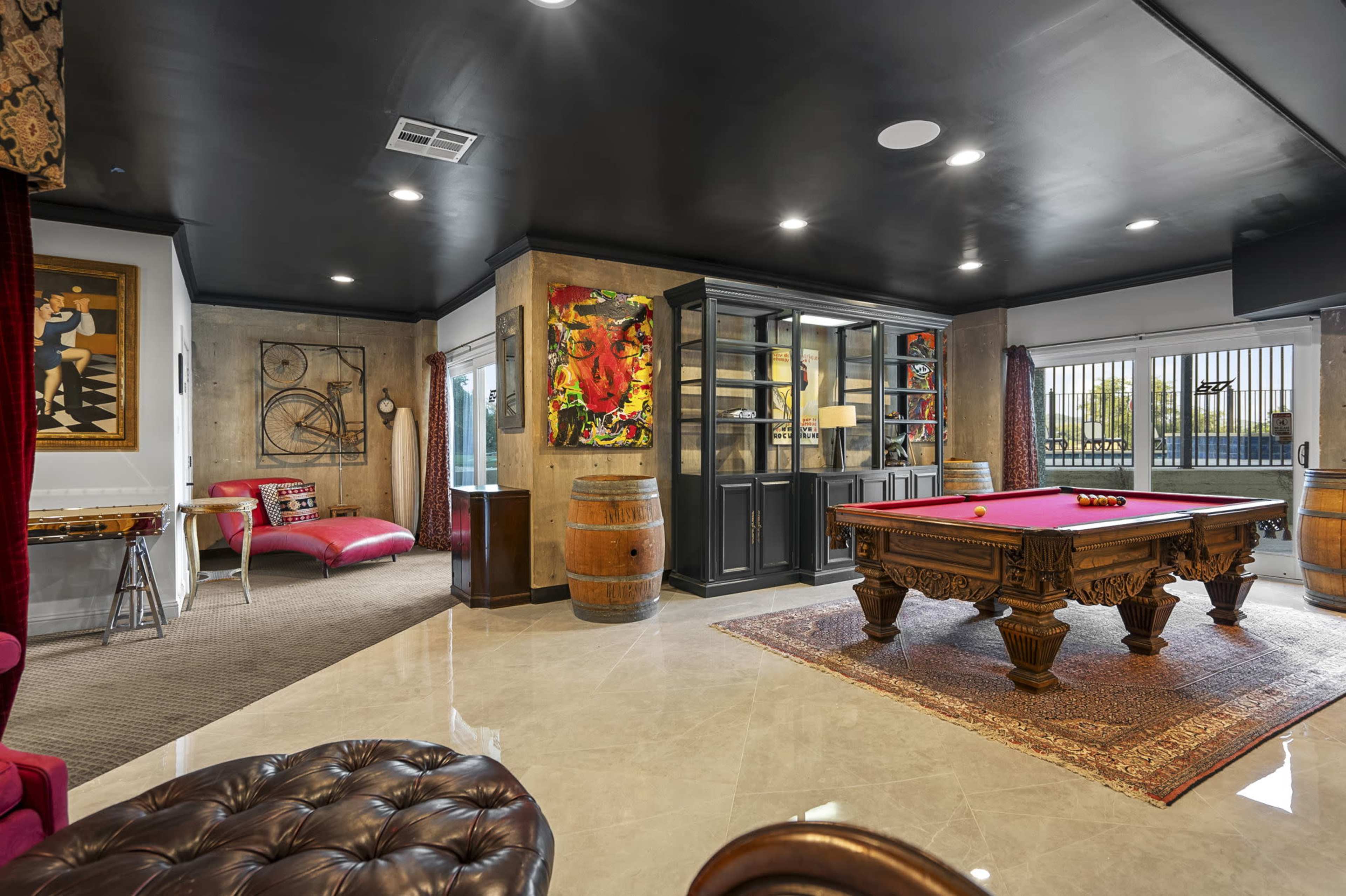 The image showcases a spacious game room featuring a pool table, a stylish seating area, and decorative artwork on the walls.