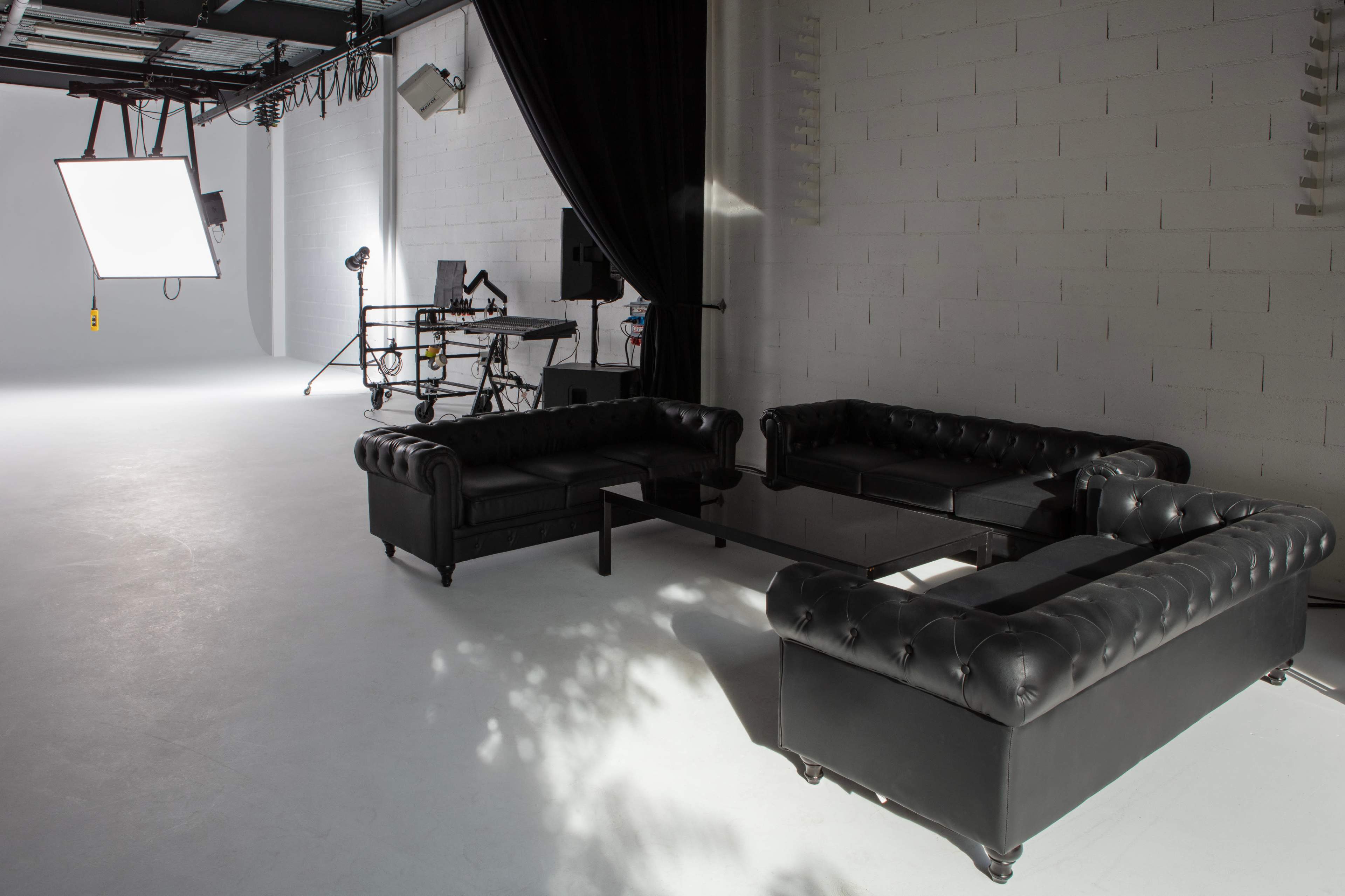 A photography studio with black leather couches arranged around a glass table and lighting equipment in the background.