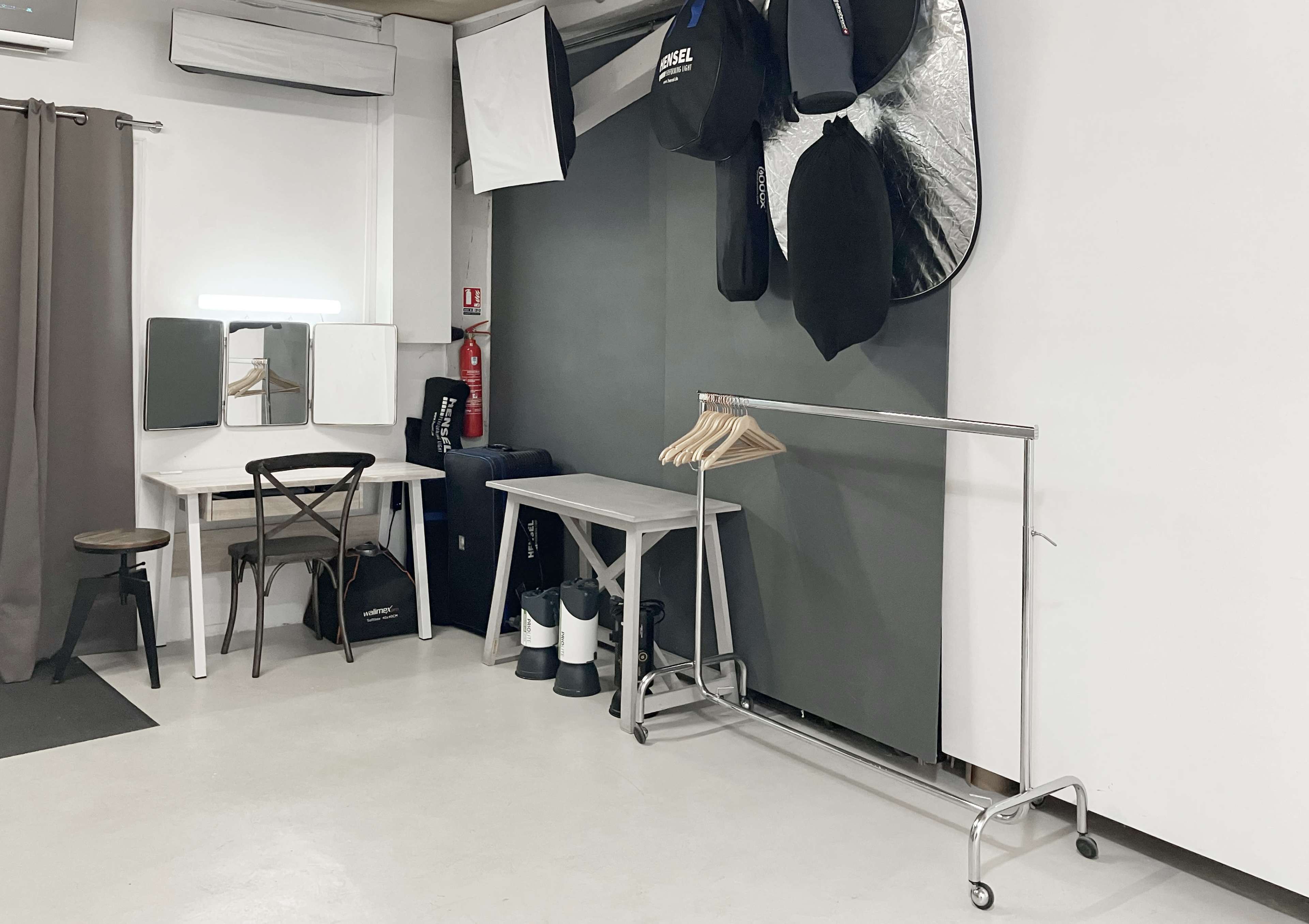 A minimalist photography studio featuring a table, chairs, a clothing rack, and various photography equipment mounted on the wall.