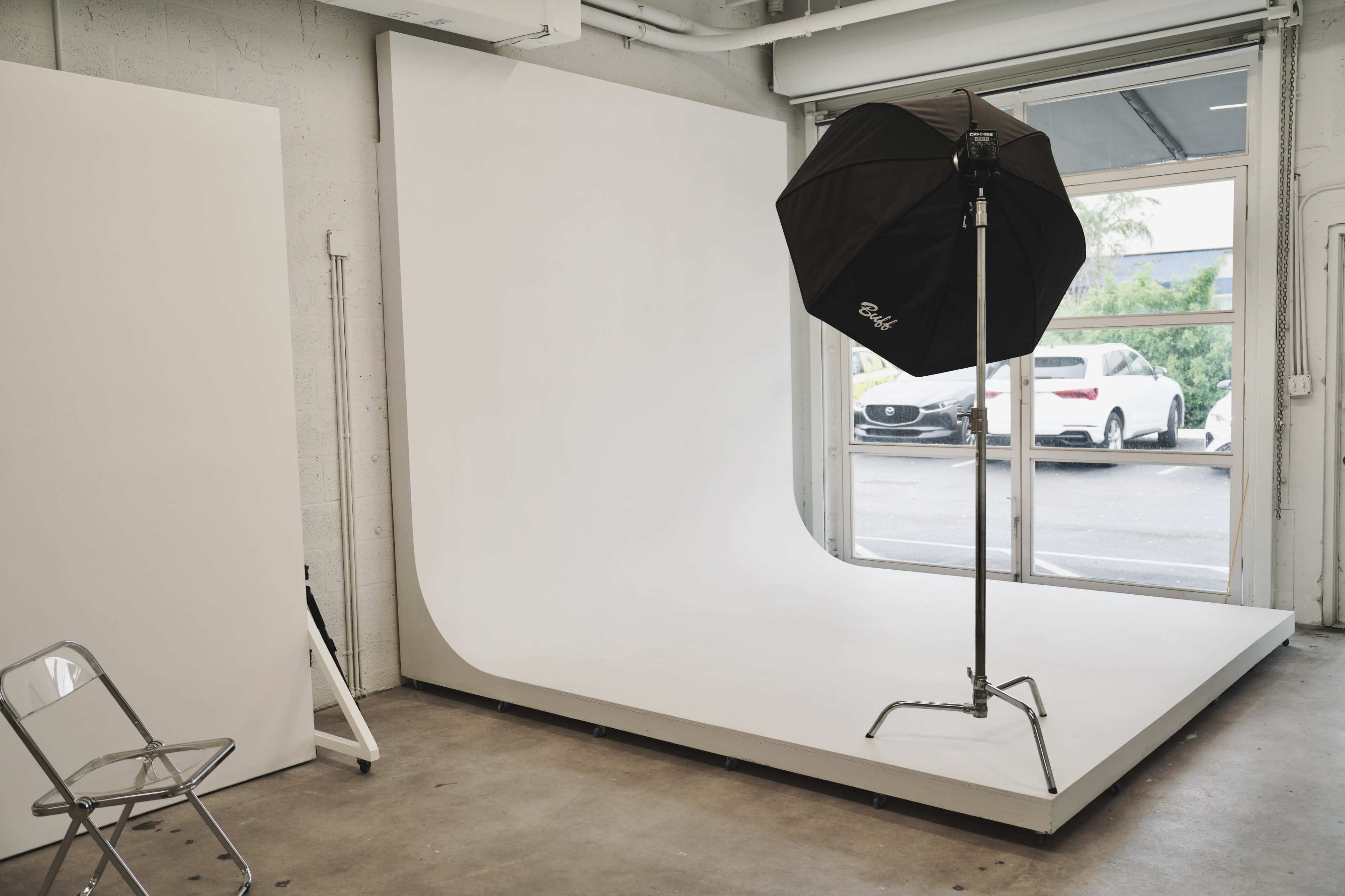 A photography studio with a large, seamless white backdrop, a light umbrella on a stand, and a folding chair.