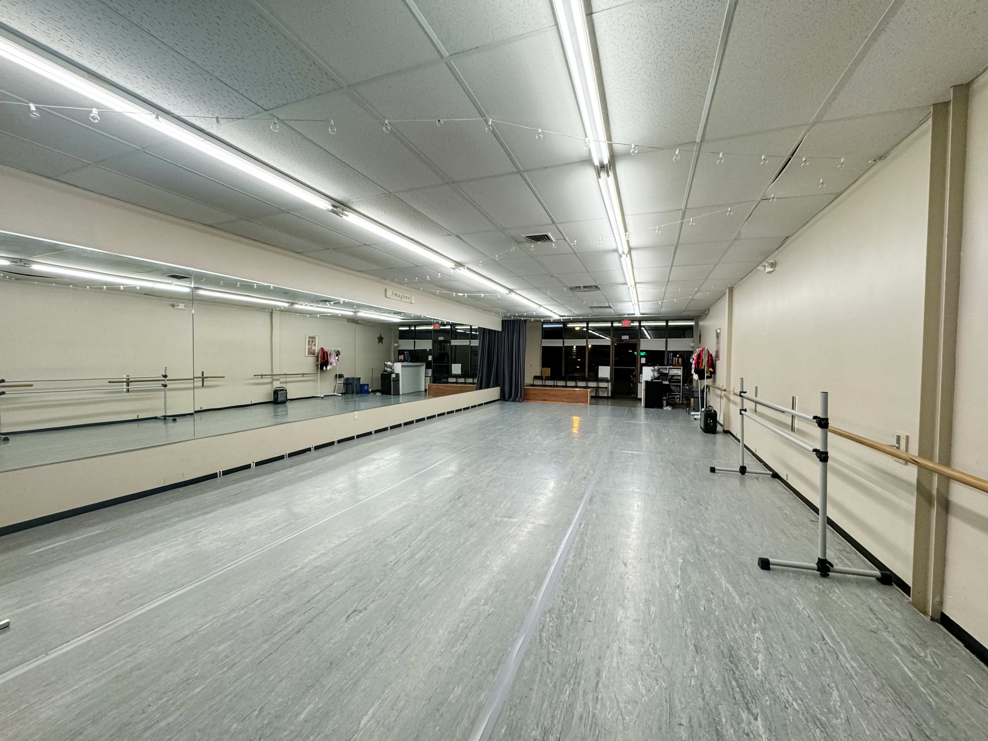 The image shows a spacious dance studio with a polished floor, mirrors along one wall, and ballet barres on the opposite side.
