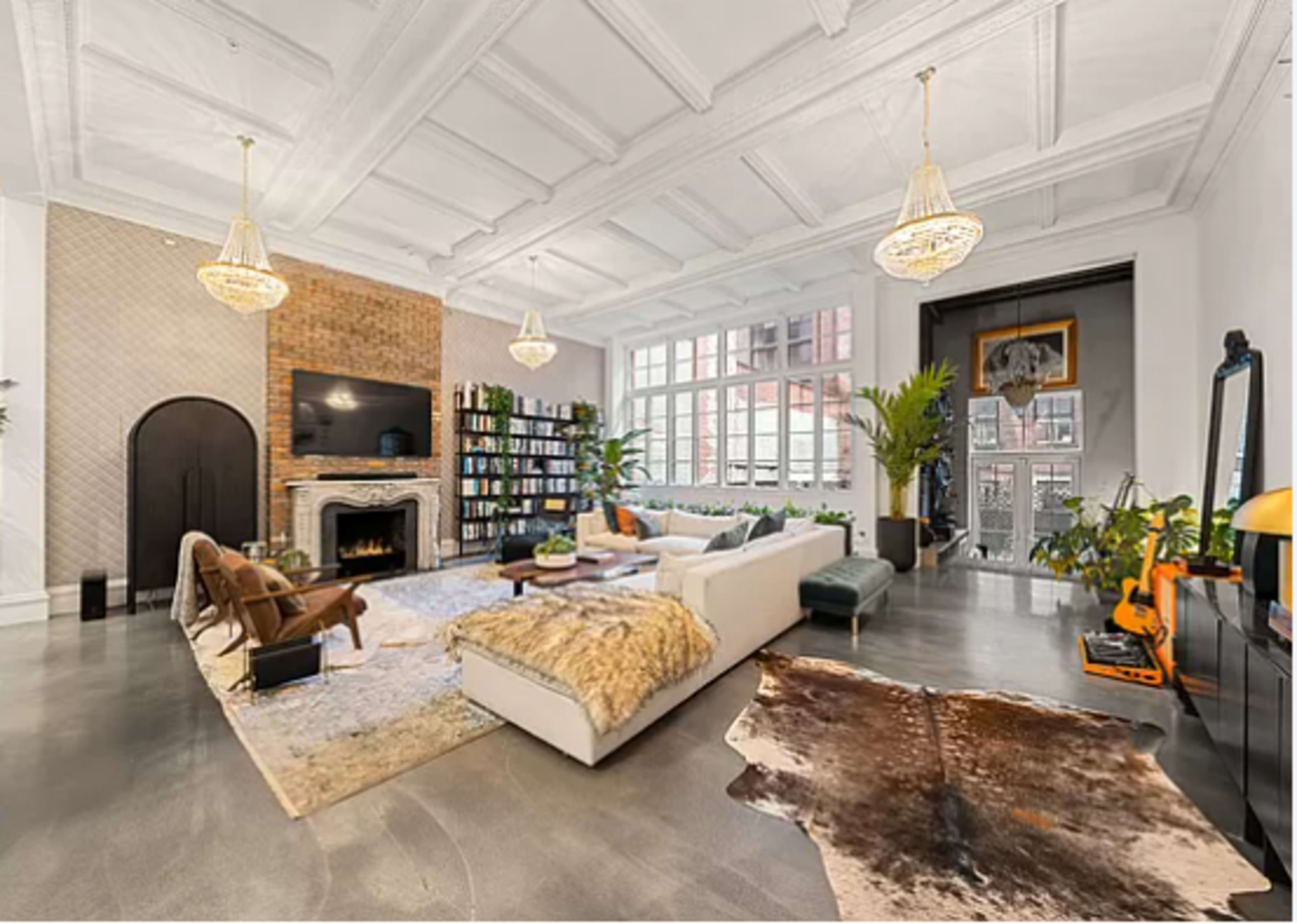 The living room features a large sofa, decorative plants, a fireplace, and a mix of modern and vintage furnishings arranged around a central area rug.