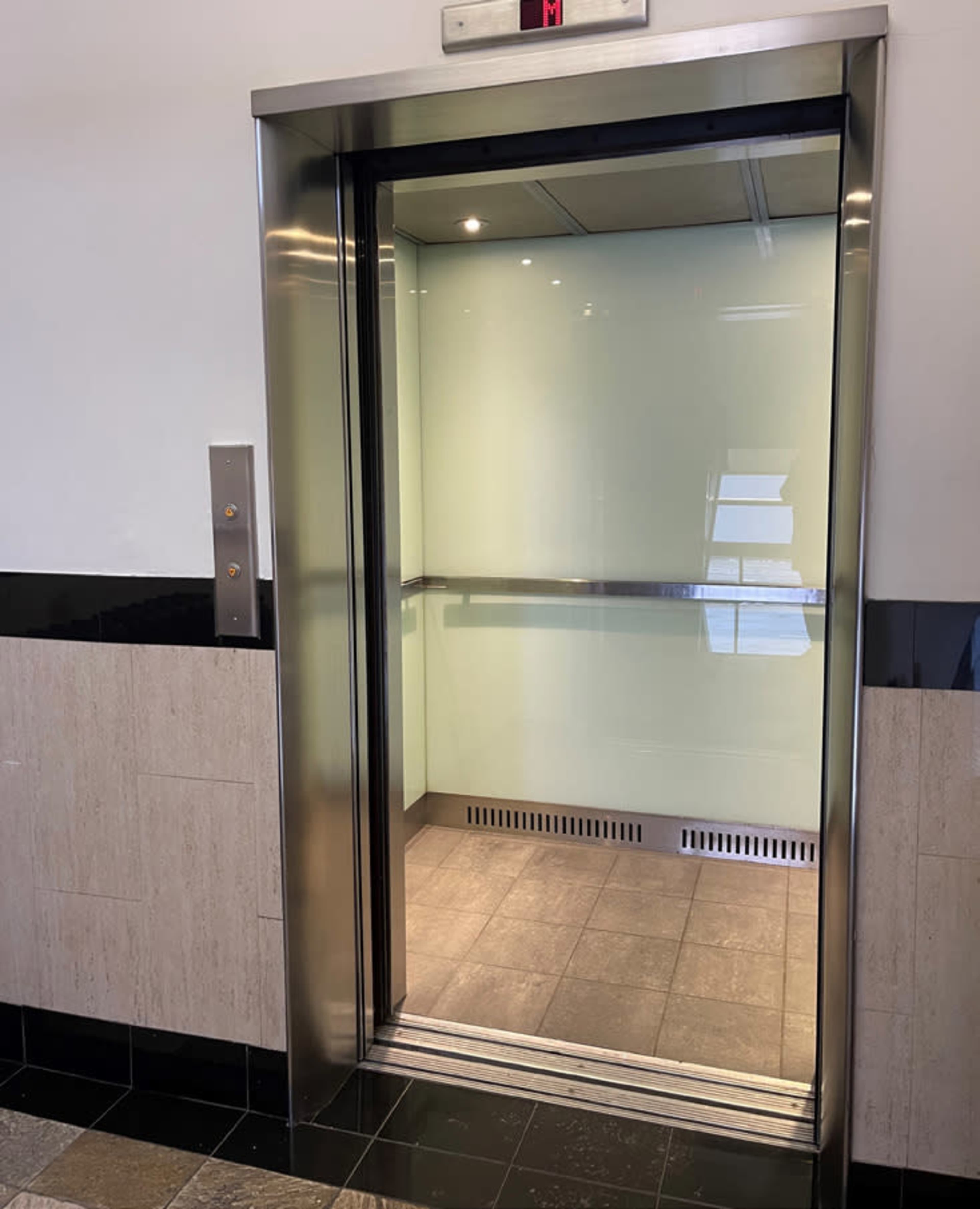 An open elevator with a glass door and tiled flooring in a modern building.