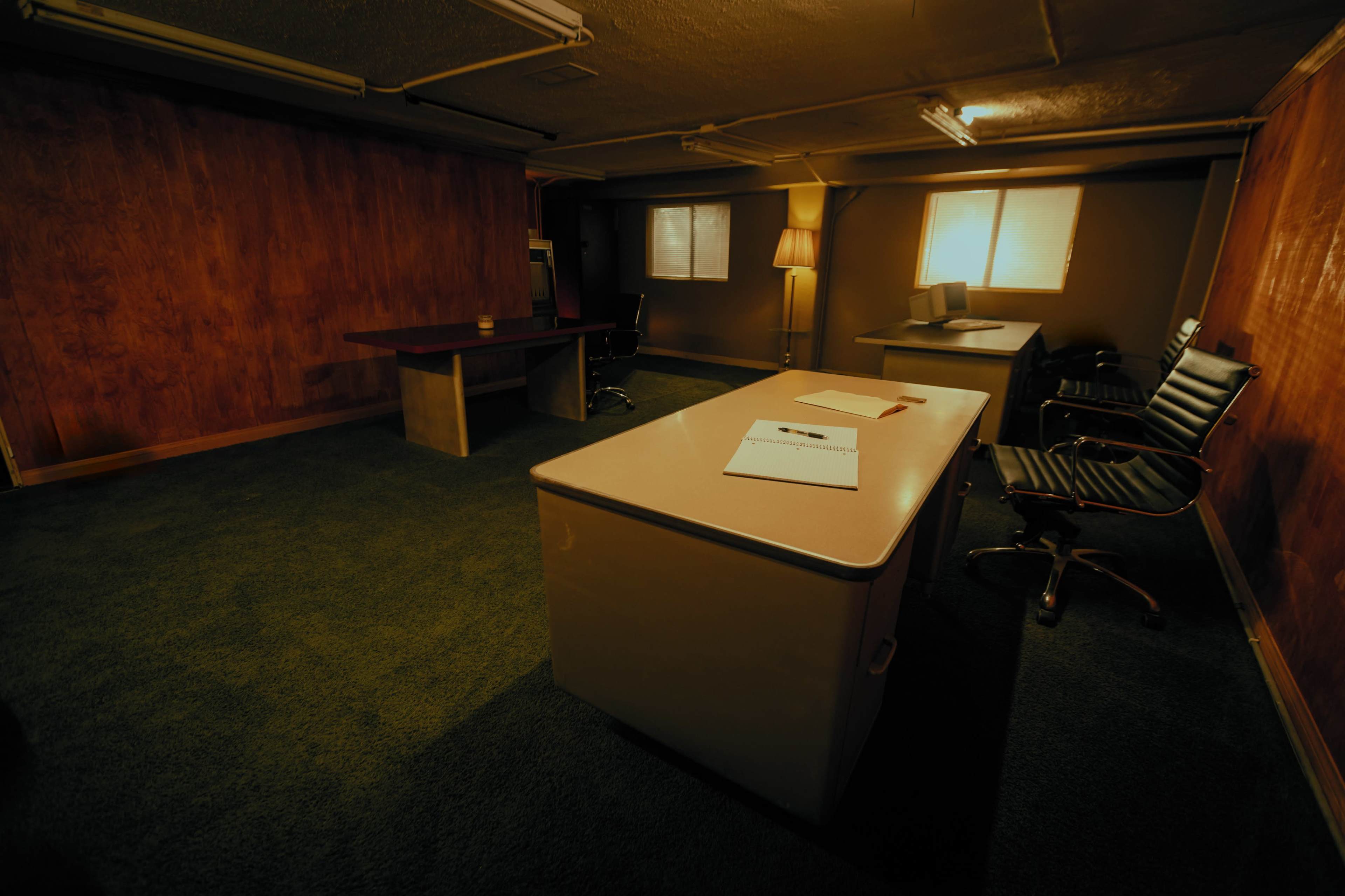 The image depicts an empty office space with a desk, two chairs, and soft lighting coming from windows.