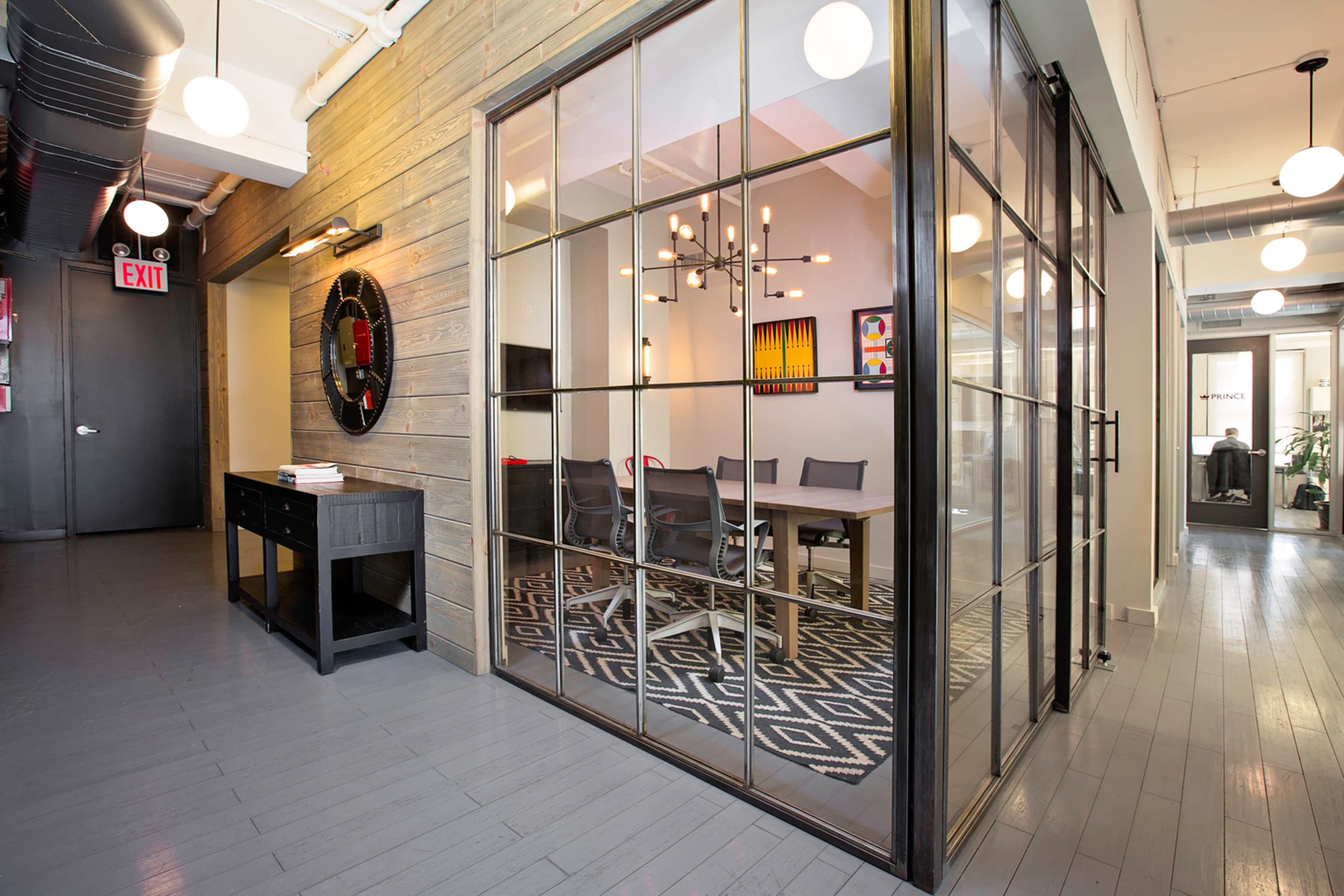 The image shows a modern office space featuring a glass-walled meeting room with a large table and chairs, surrounded by wooden walls and contemporary decor.
