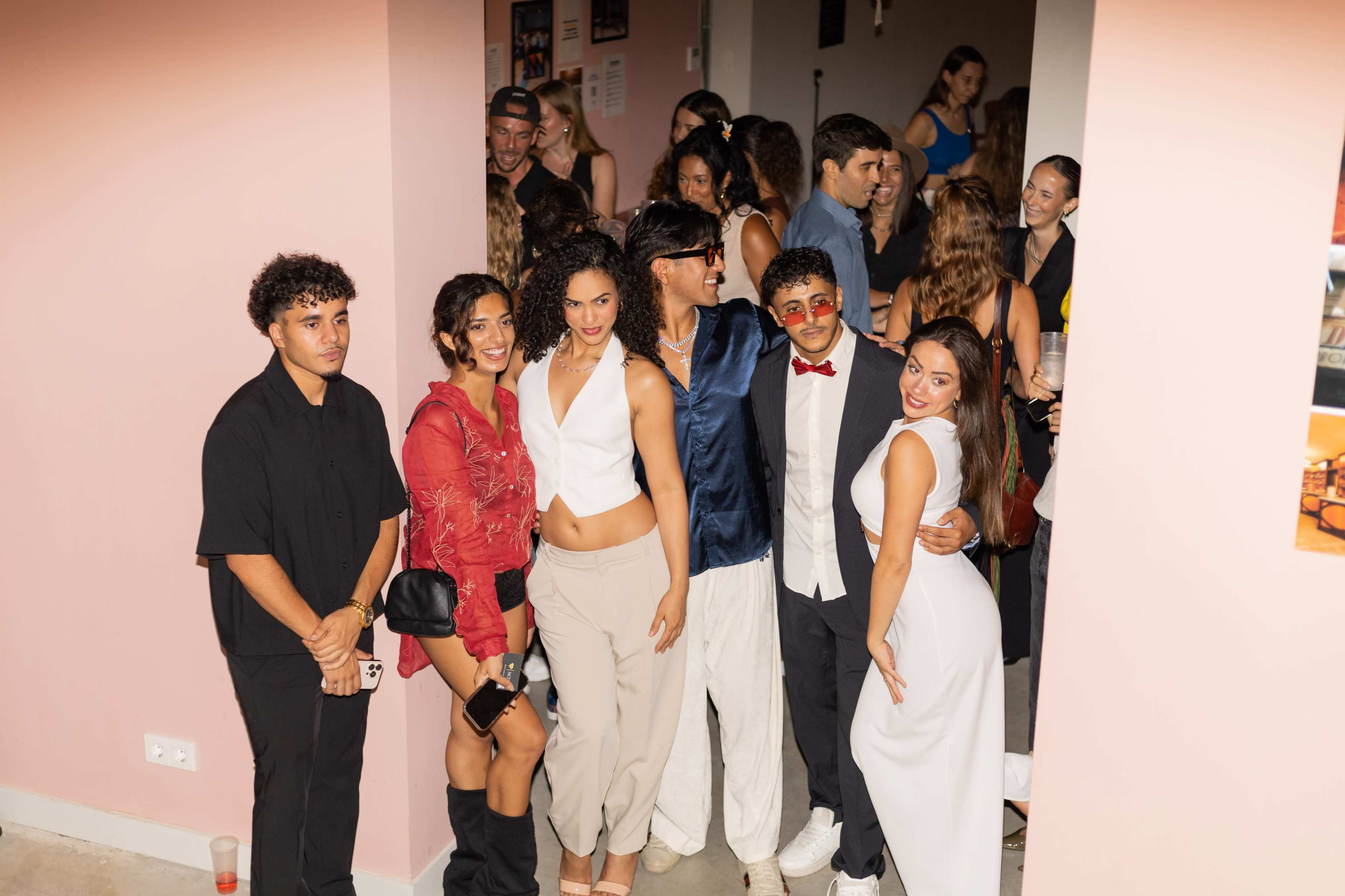 A group of six people poses together in a brightly lit room filled with other guests.