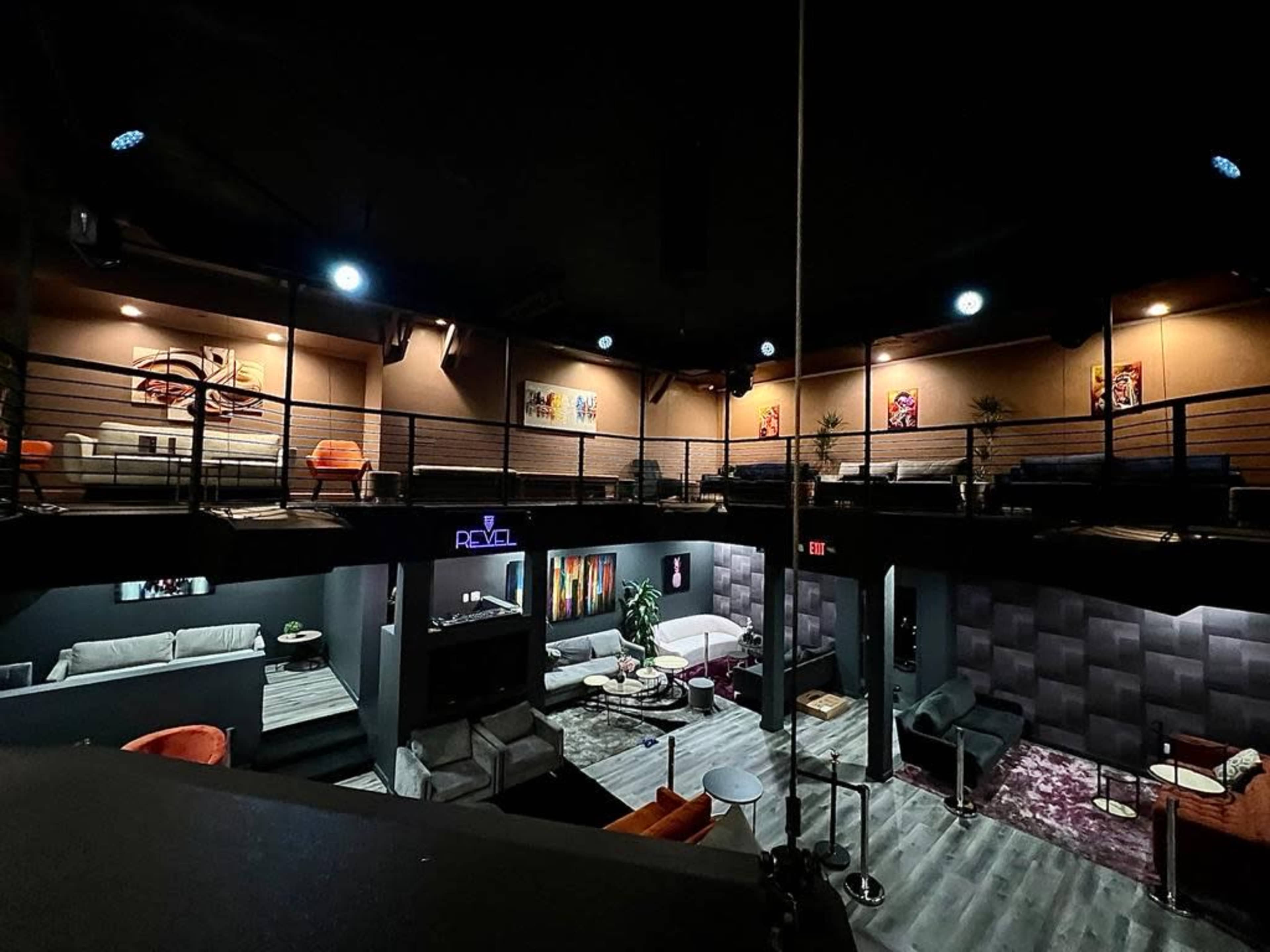 A modern, multi-level lounge with seating areas, colorful artwork on the walls, and dim lighting.