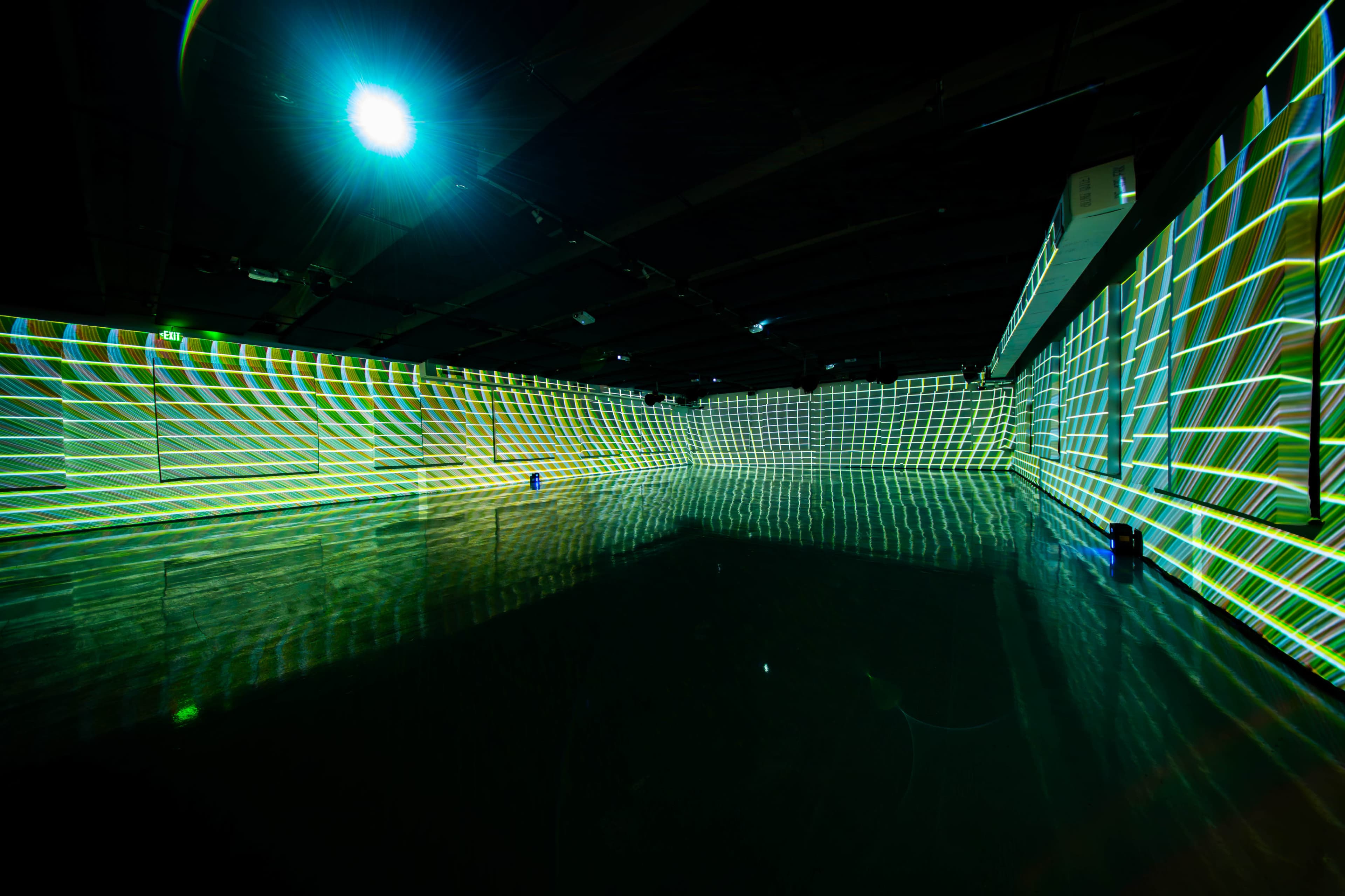 The image depicts a spacious, dark room with projected green and yellow grid patterns illuminating the walls and floor.