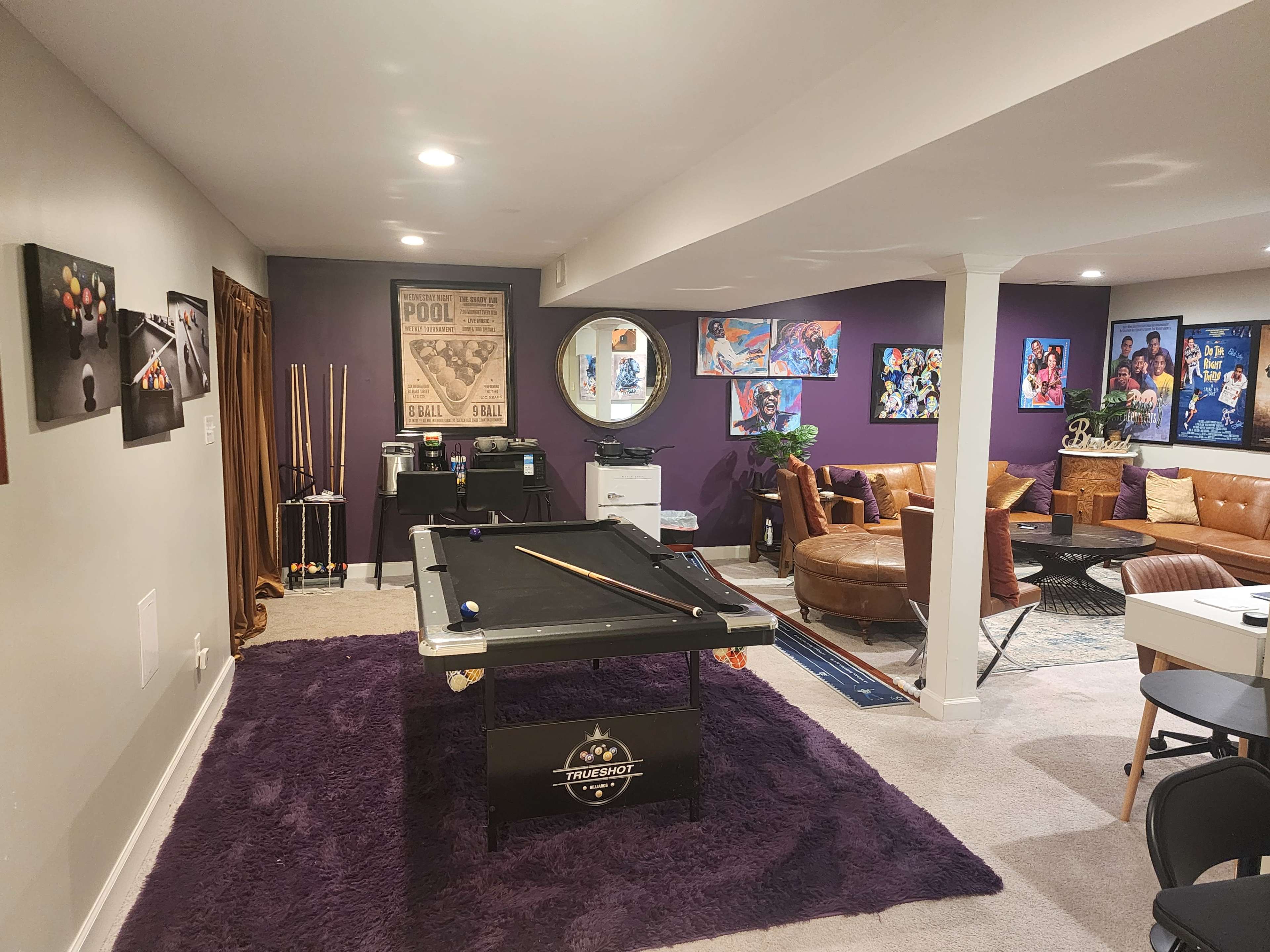 The image shows a stylish game room with a pool table, colorful artwork on the walls, and a cozy seating area.