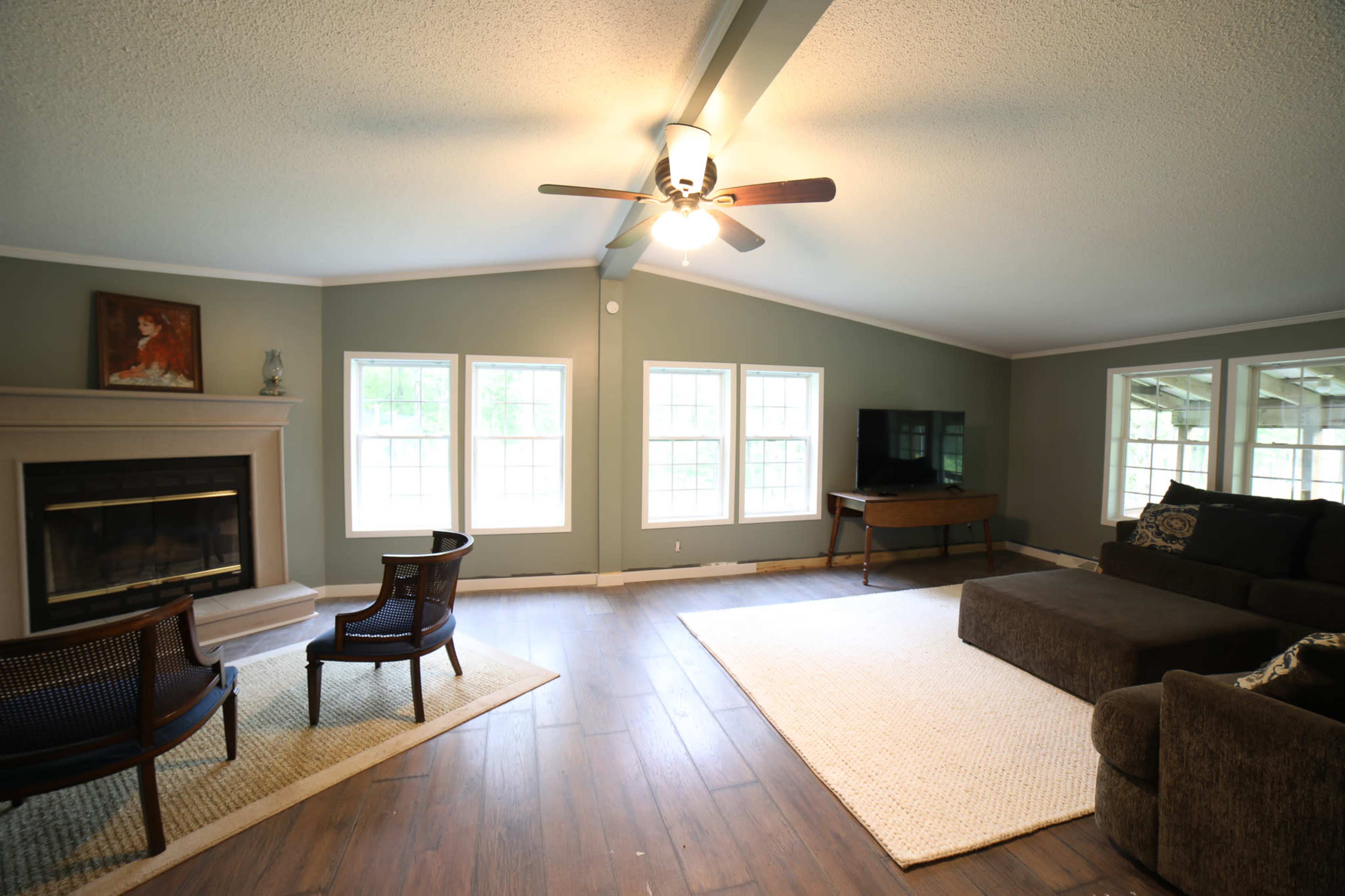 The living room features a fireplace, two chairs, a sectional sofa, and large windows that provide natural light.