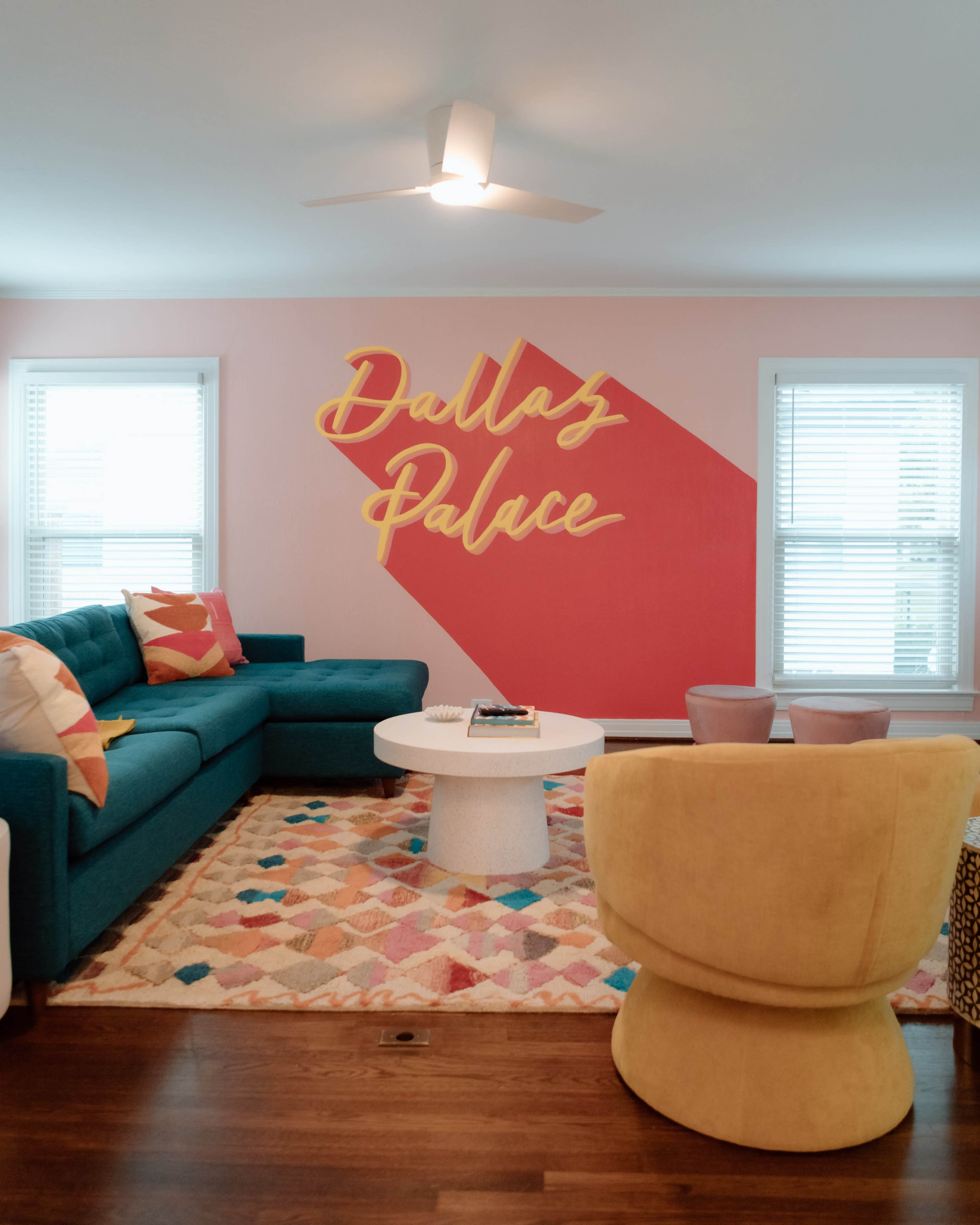 The living room features a teal couch, a round white coffee table, and a vibrant wall mural with the text "Dallas Palace."