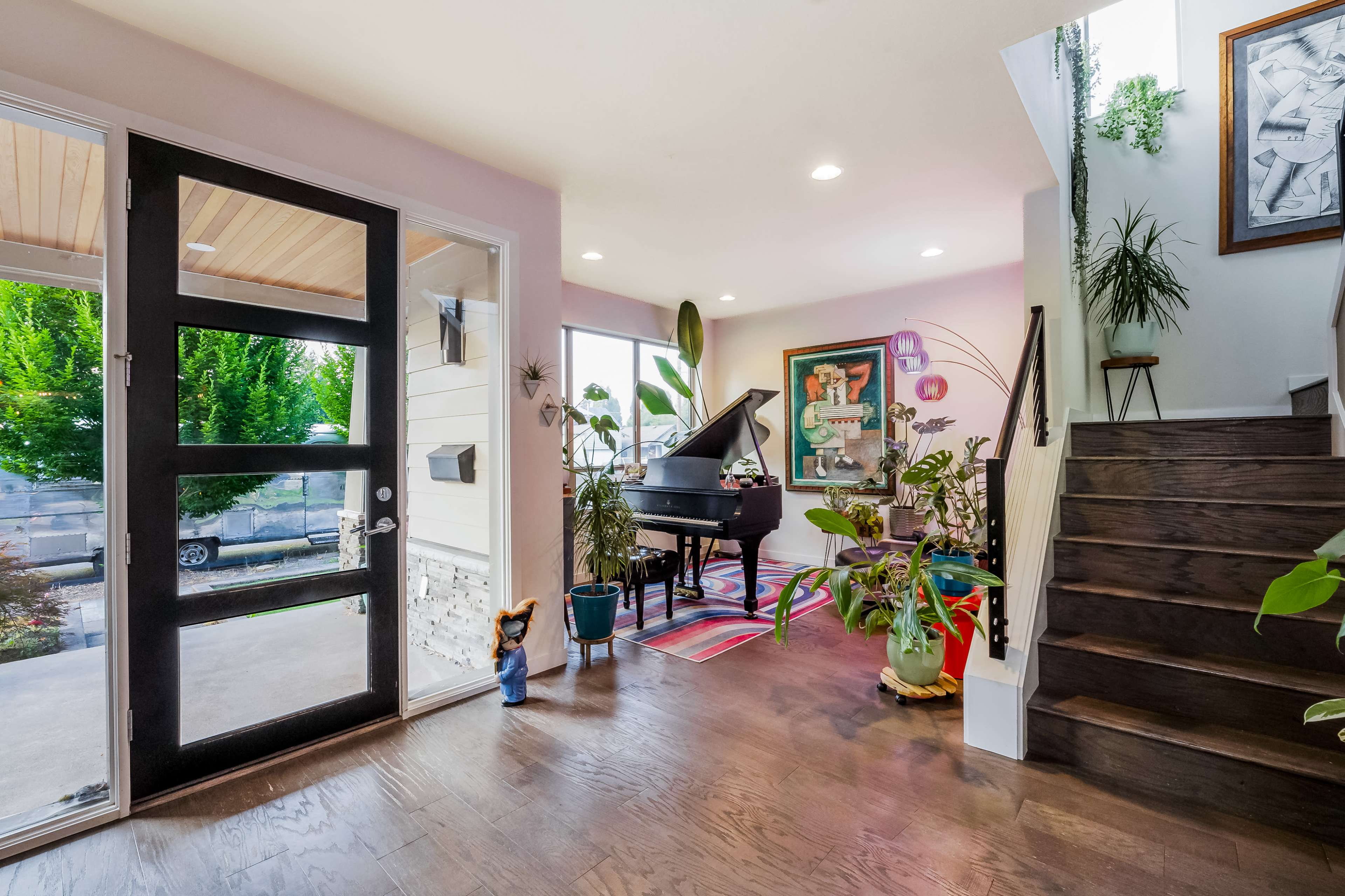A spacious entryway featuring a piano, vibrant plants, and a staircase leading to an upper level.