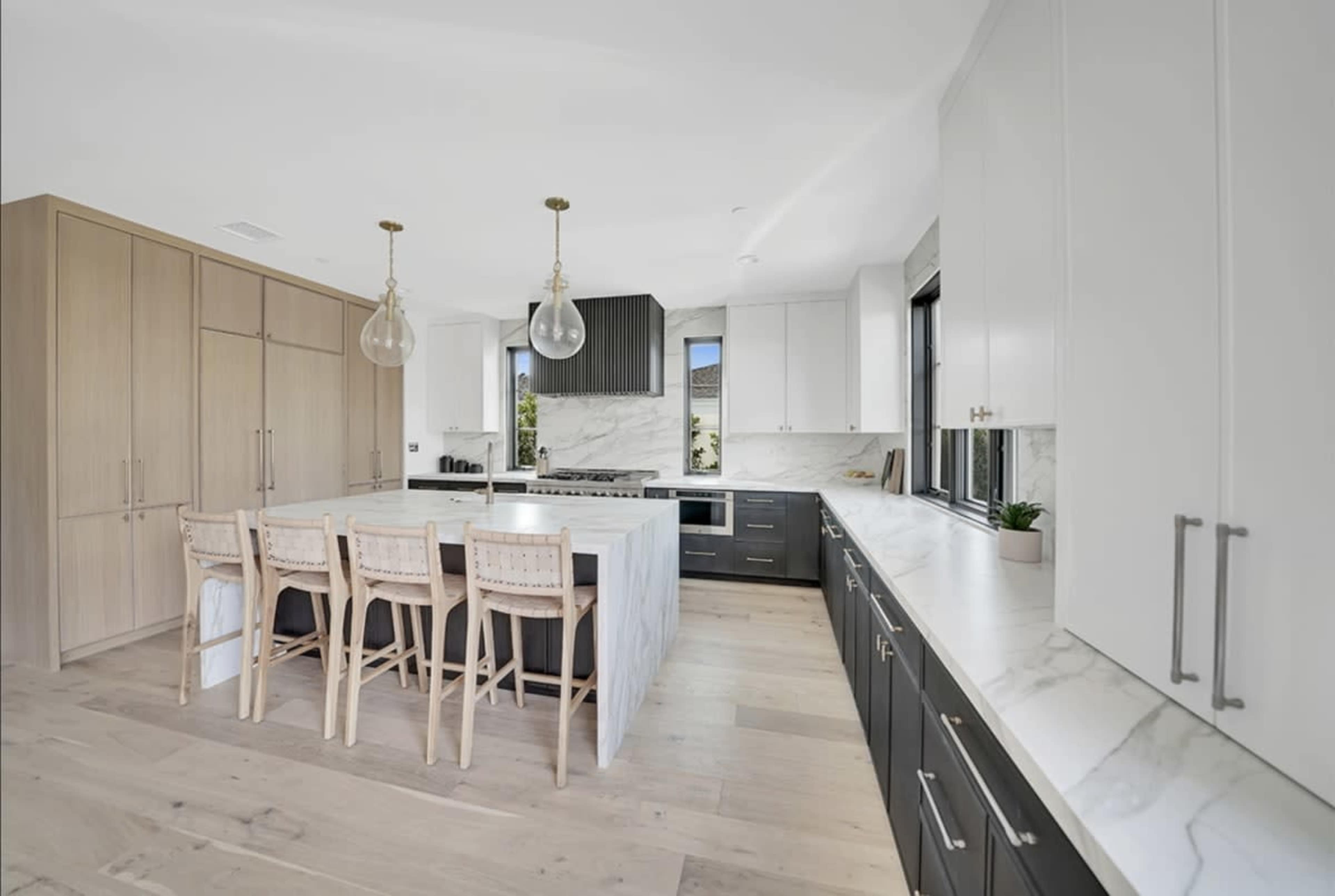 The kitchen features a large island with bar stools, marble countertops, and a combination of light wood and dark cabinetry.