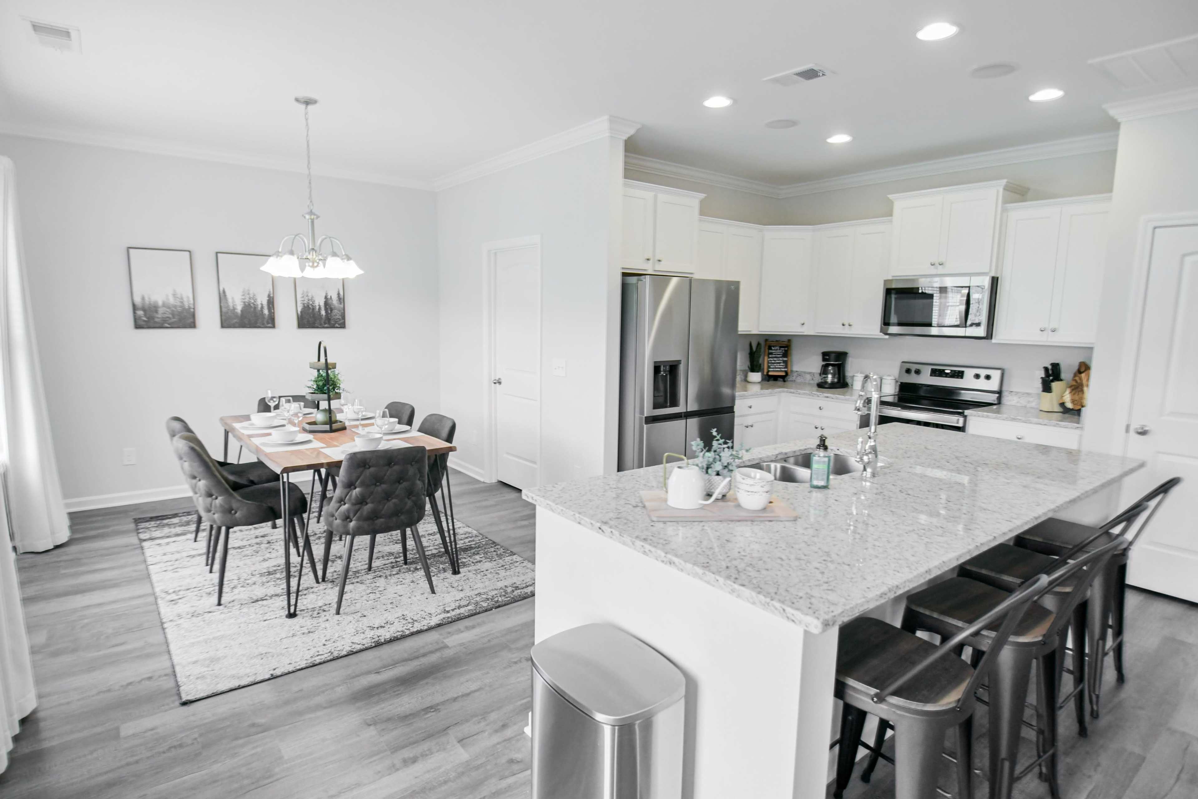 A modern kitchen with stainless steel appliances and granite countertops opens up to a dining area featuring a wooden table set for meals.