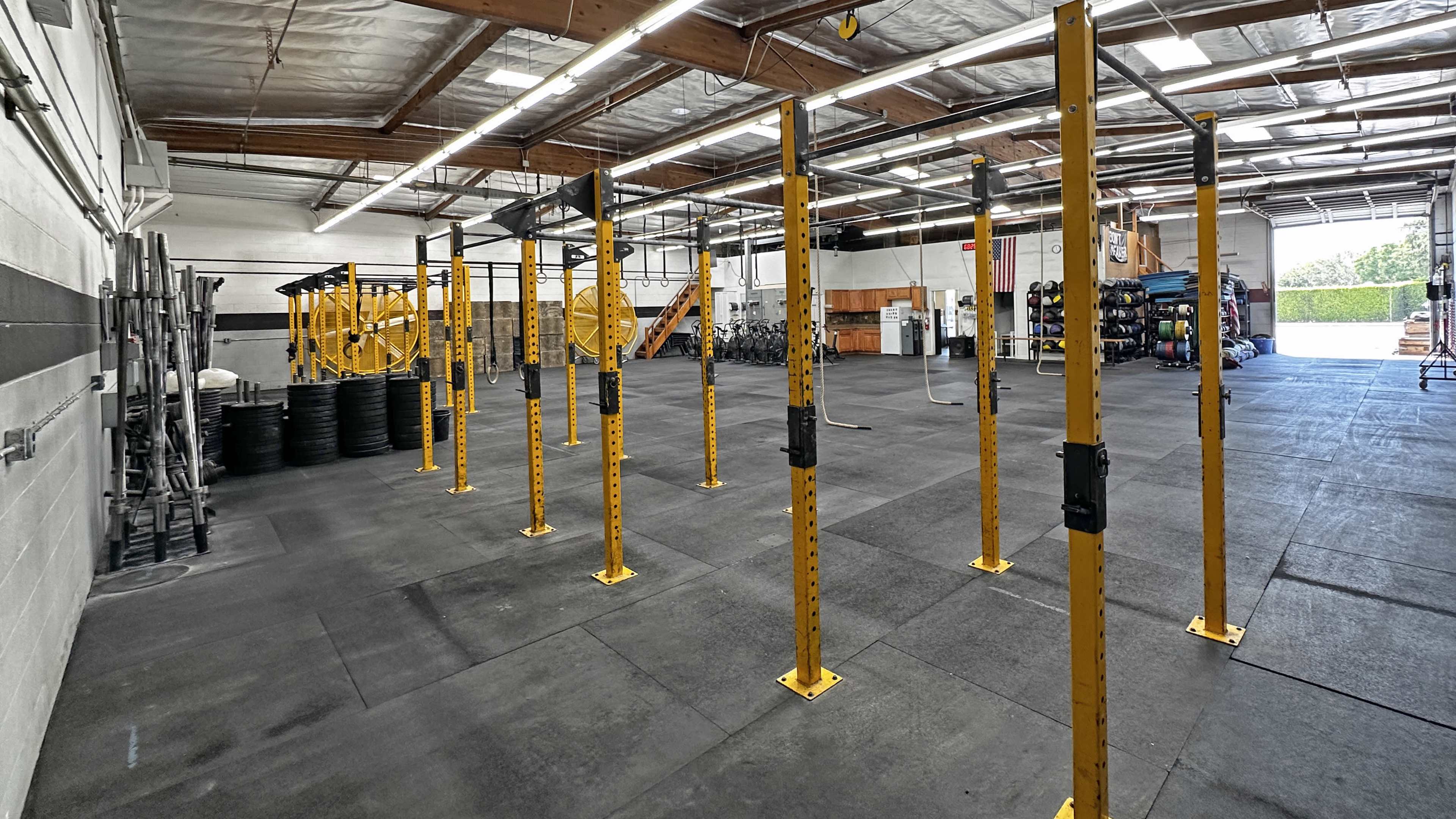 The image shows a spacious gym with yellow workout equipment, black weightlifting plates, and a smooth floor, featuring various exercise stations in a well-lit environment.