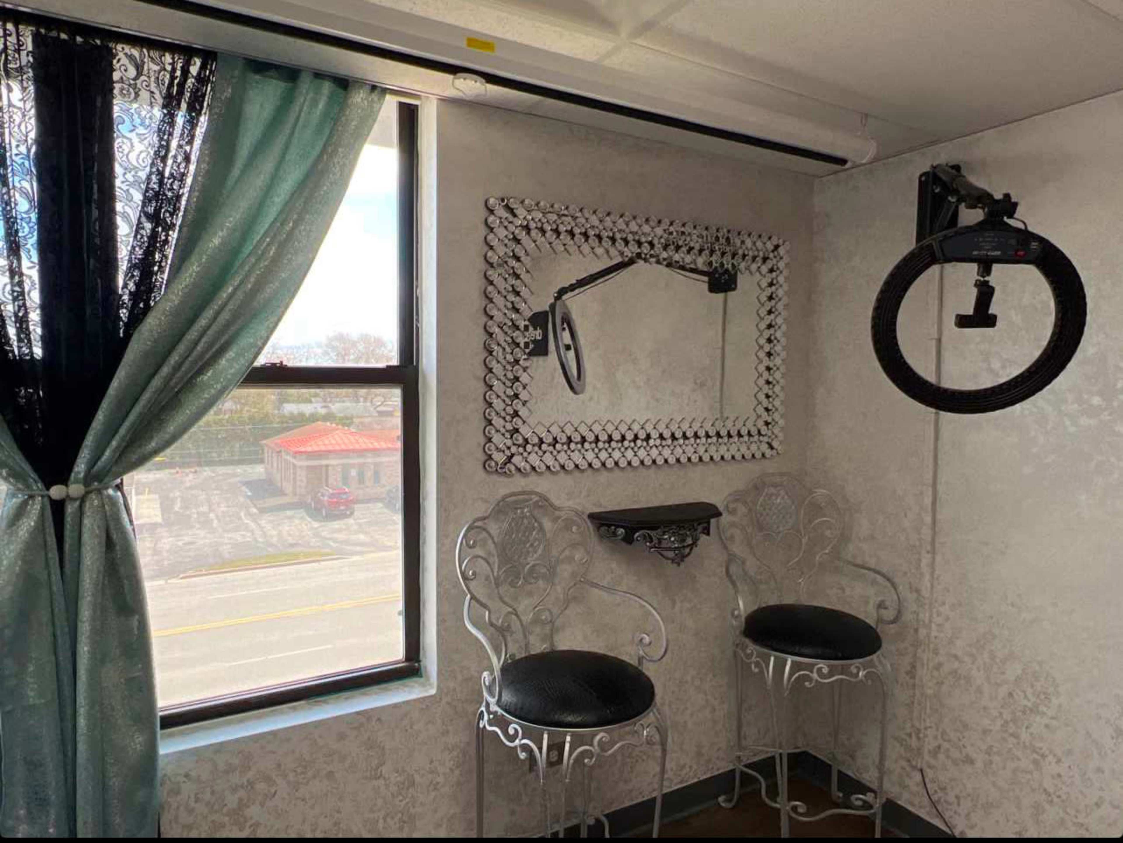 The image shows a small room with two chairs, a mirror mounted on the wall, and a ring light hanging above.