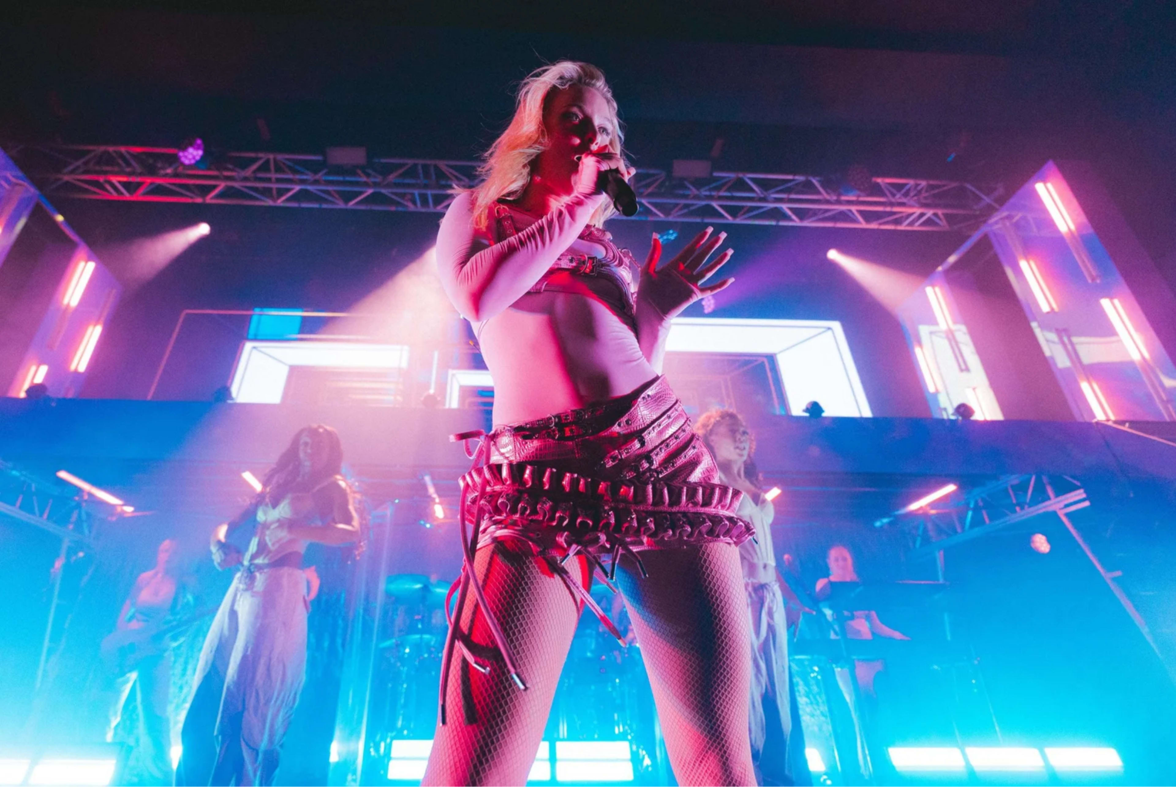 A performer sings on stage while surrounded by colorful lights and backup dancers.