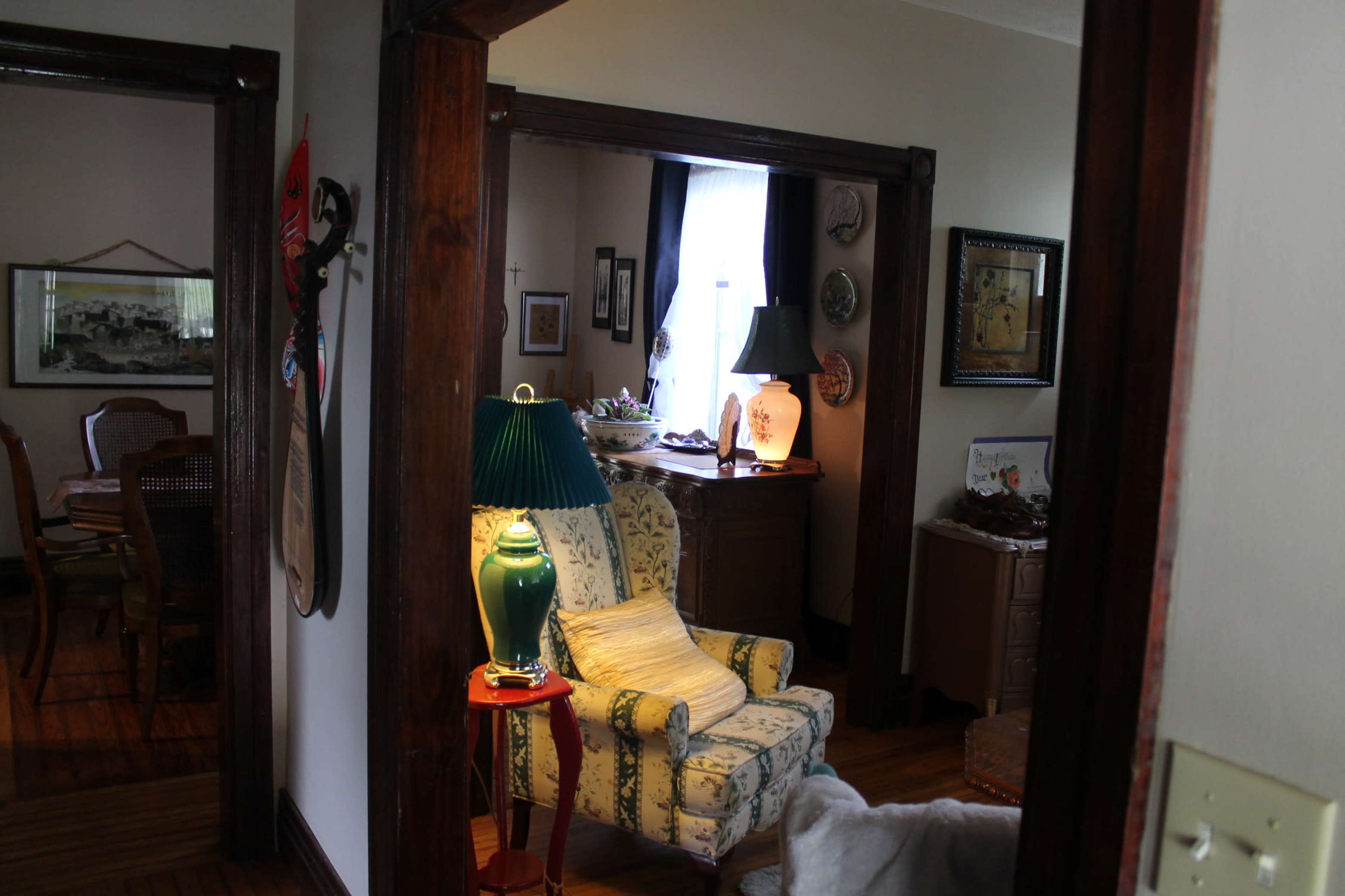 A cozy room with a patterned armchair, a green lamp on a side table, and various decorative items in the background.