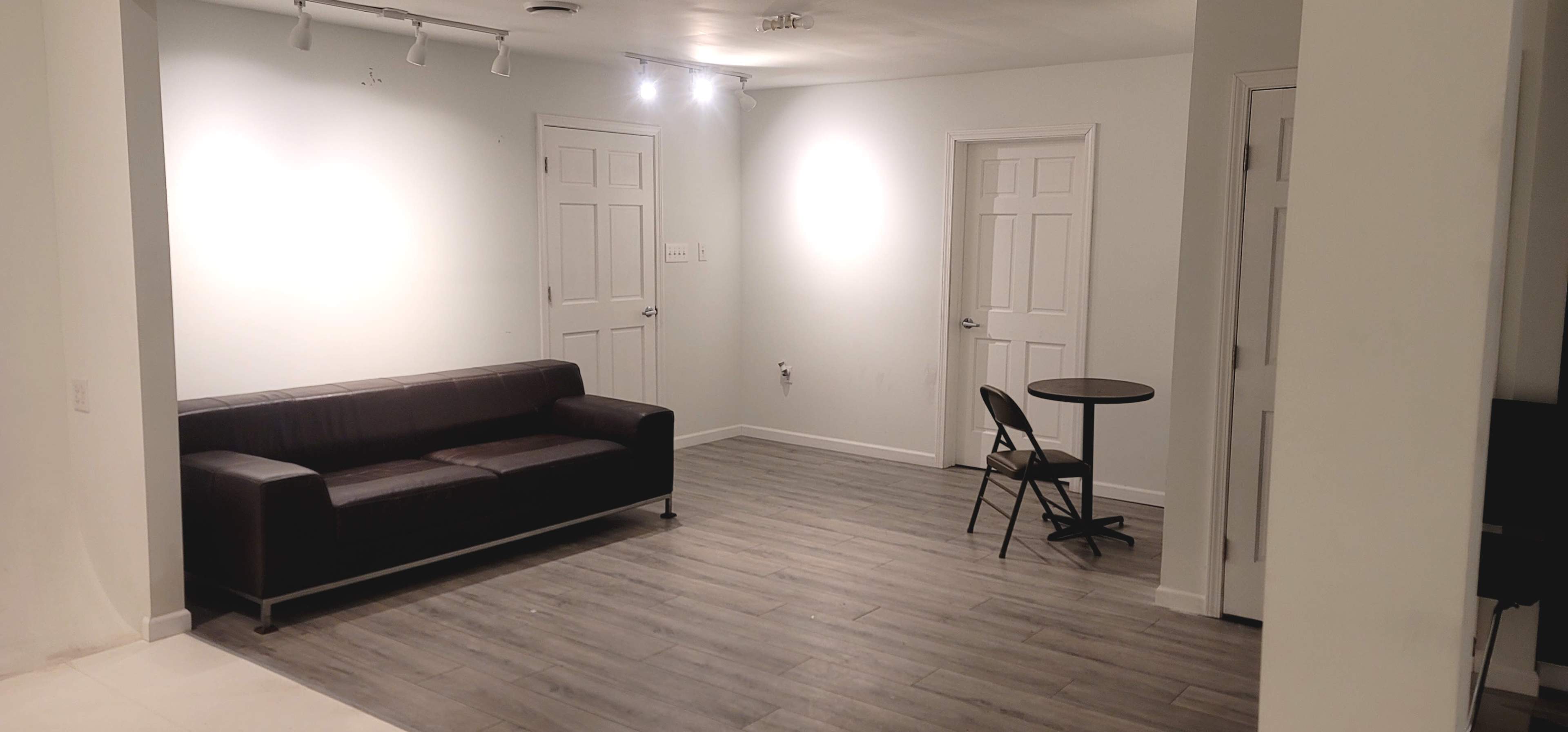 A sparsely furnished room with a black sofa, a small round table, and two closed doors on opposite walls.