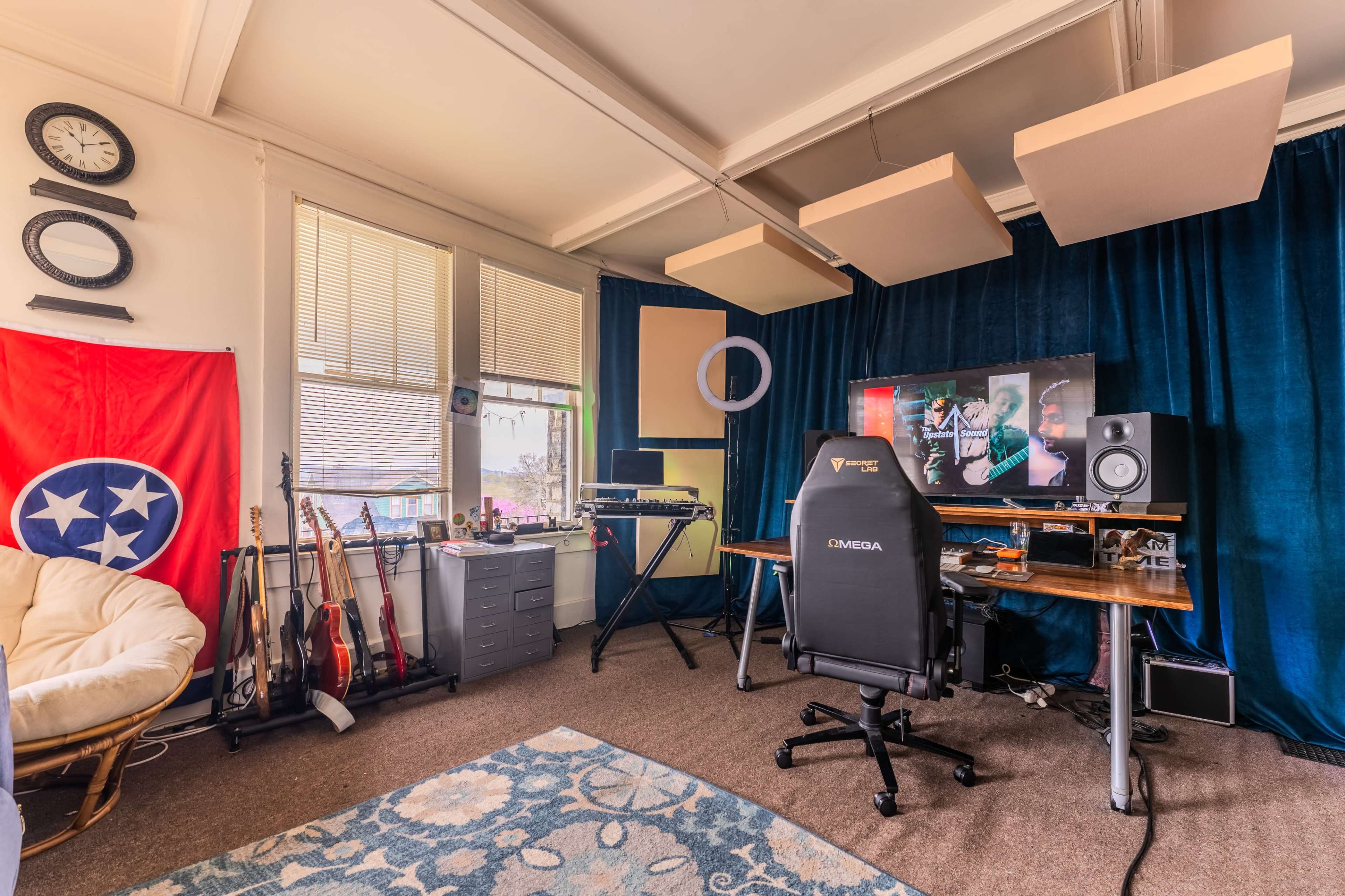 A home office featuring a desk with a computer setup, a comfortable chair, musical instruments, a Tennessee flag, and sound panels on the ceiling.