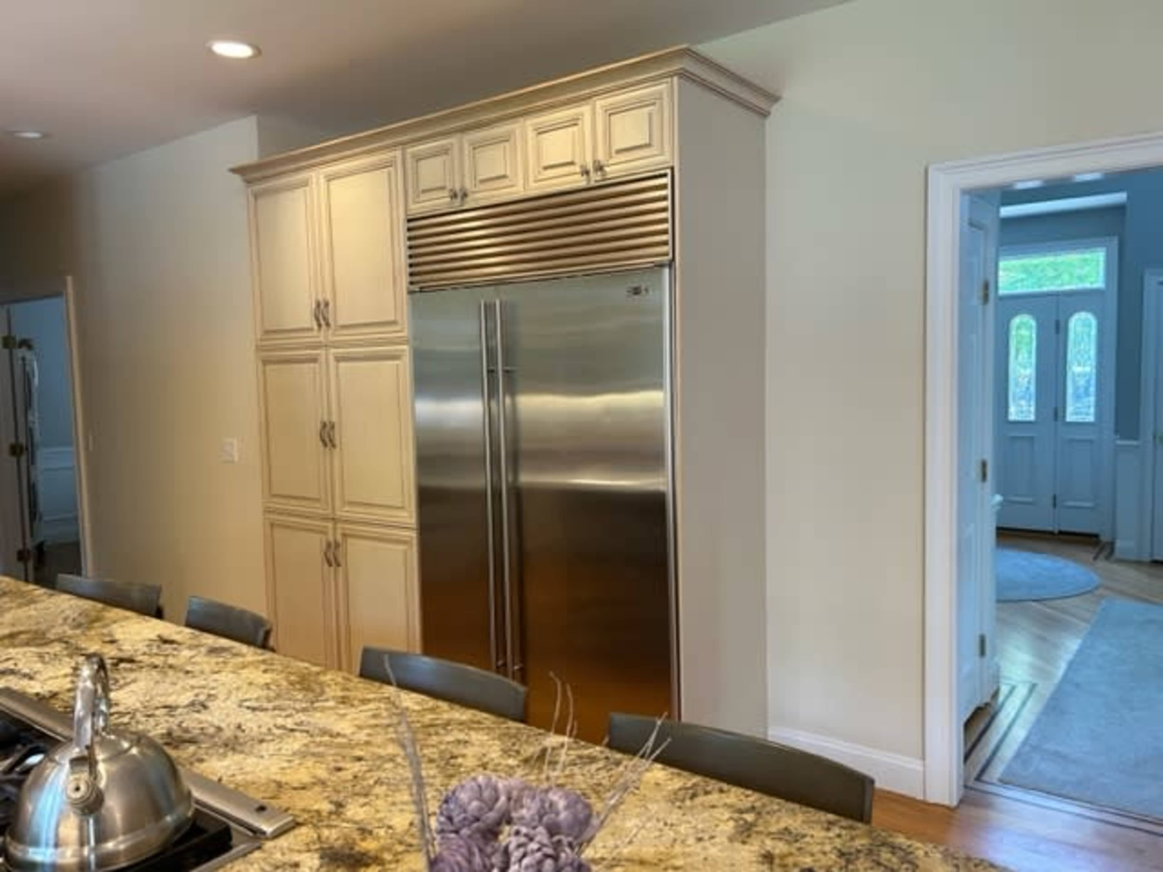A modern kitchen with a large stainless steel refrigerator, cabinetry, and a granite countertop with seating.