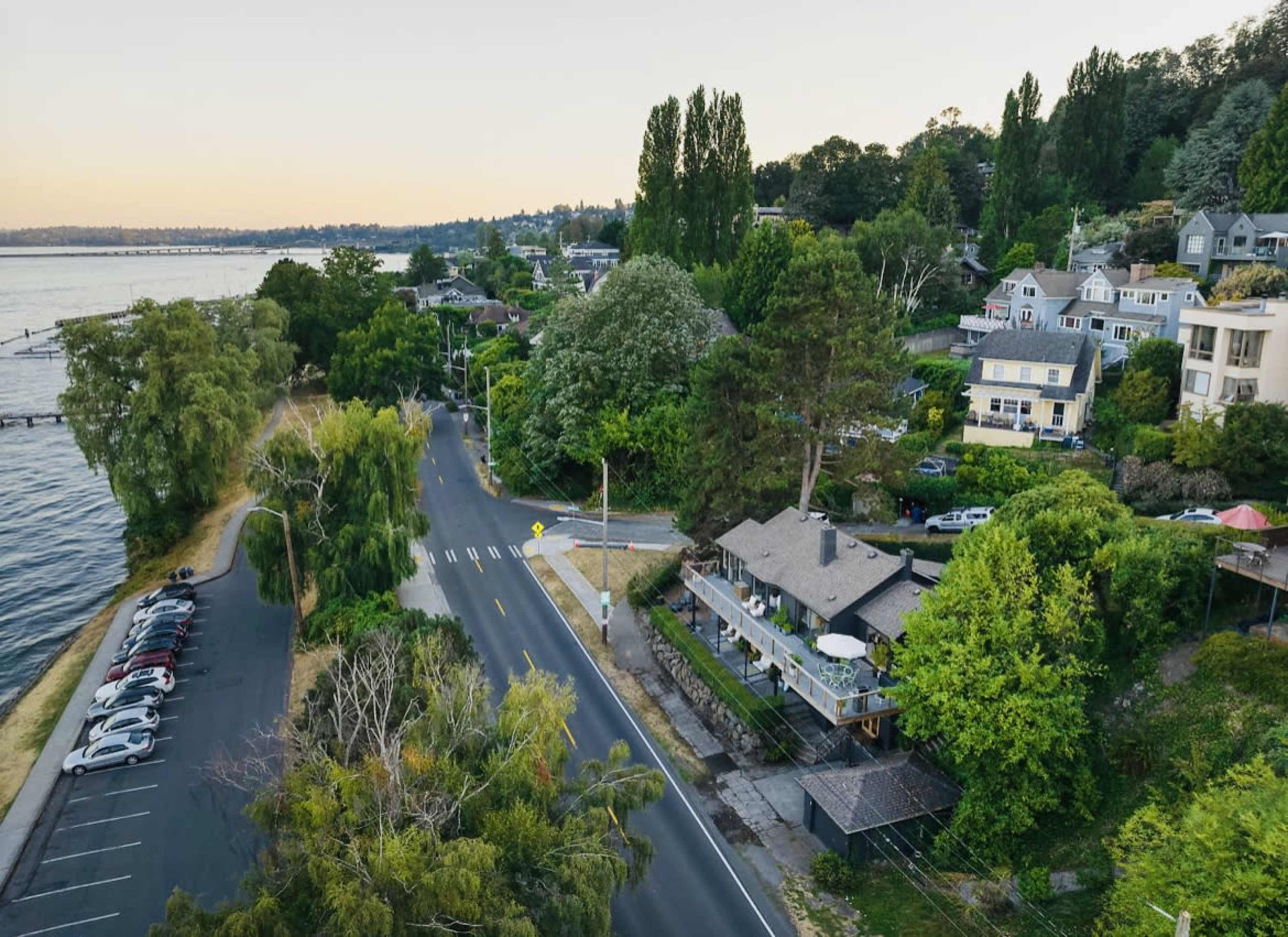 A waterfront neighborhood with houses, trees, and a road lined by greenery.