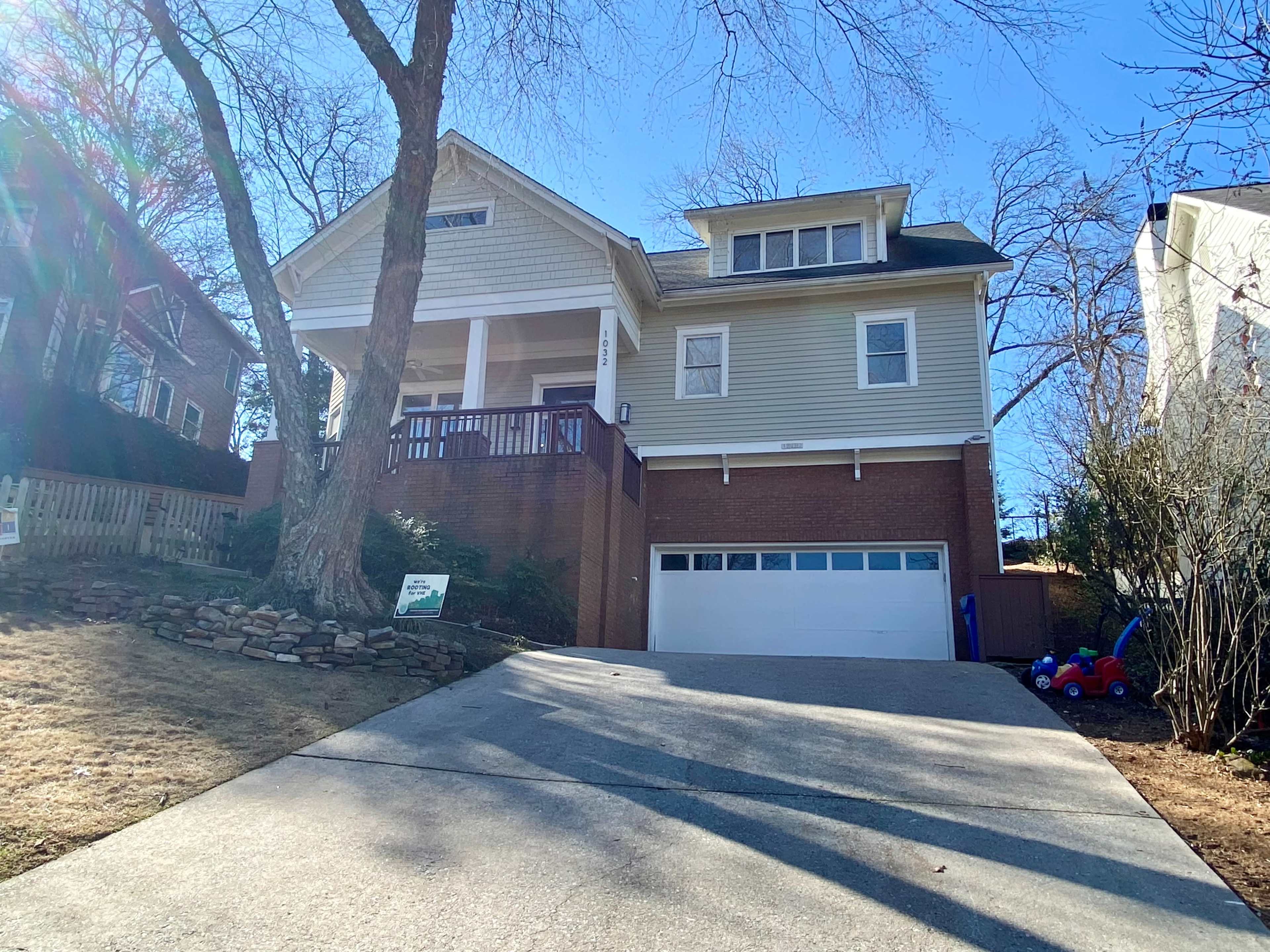 The image shows a two-story house with a front porch, a garage, and a driveway leading up to it, situated on a sloped lot.