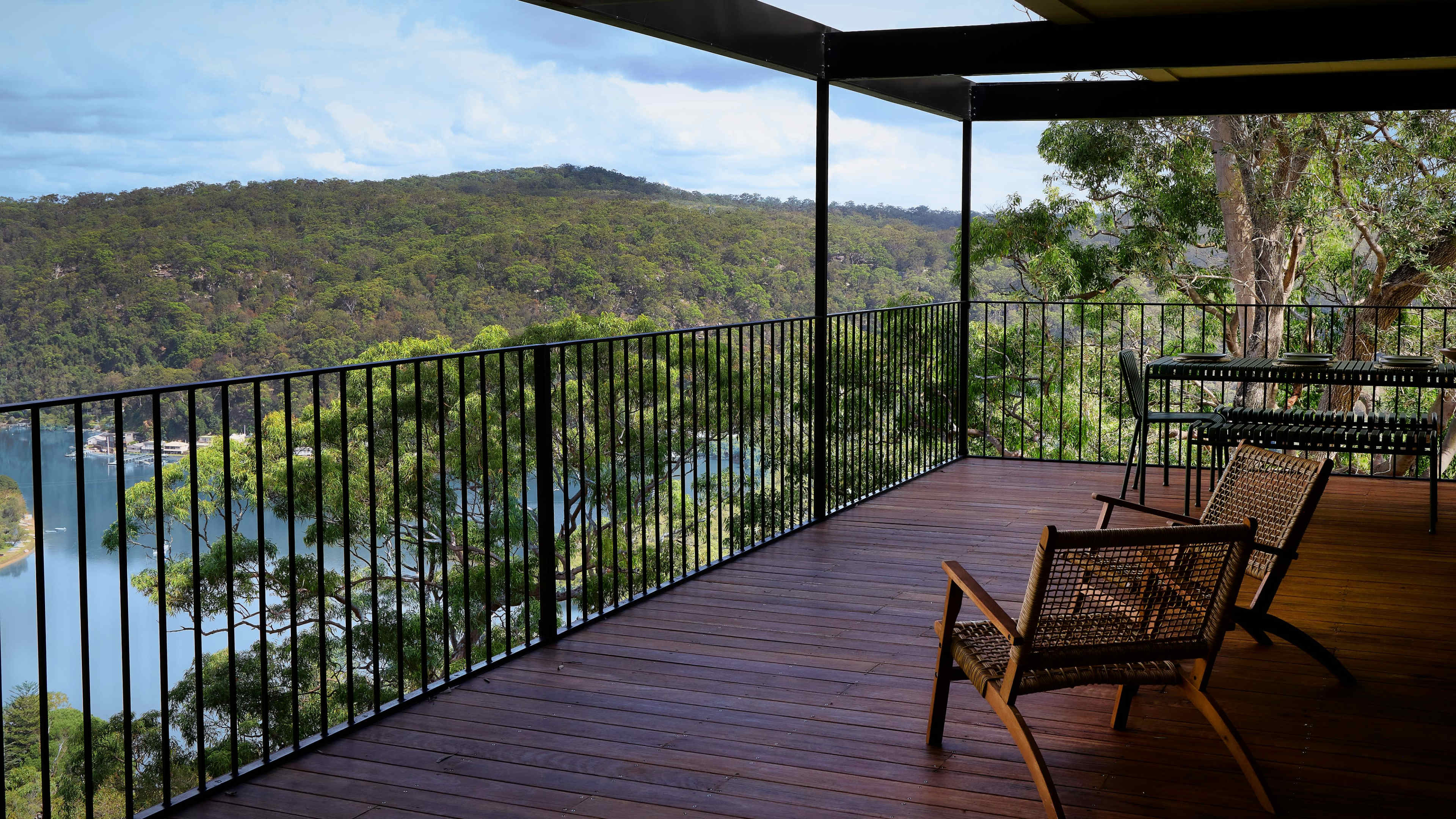 A wooden deck with two chairs overlooks a lush, green valley and a river below.