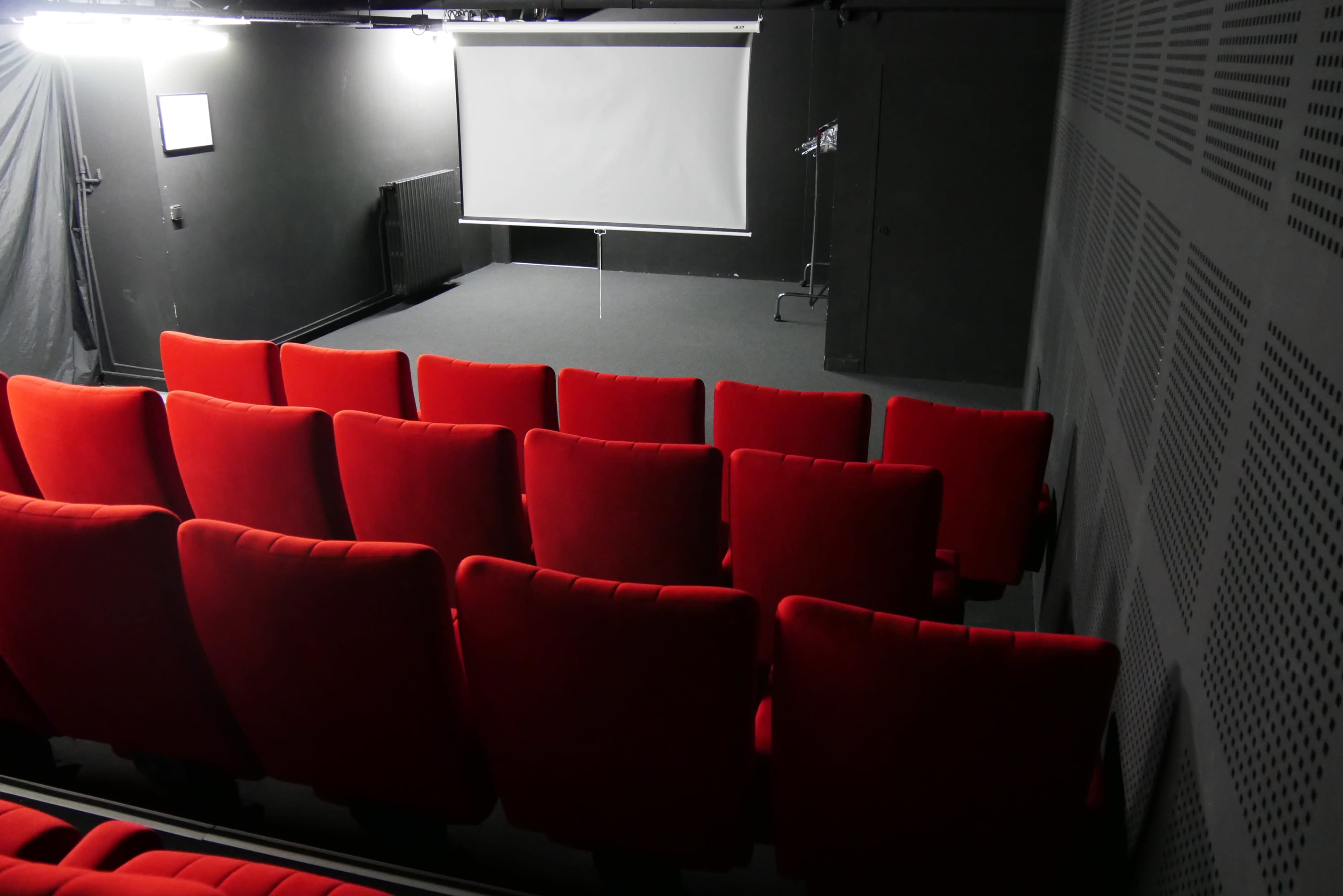 A small theater space with red seating facing a blank projection screen.