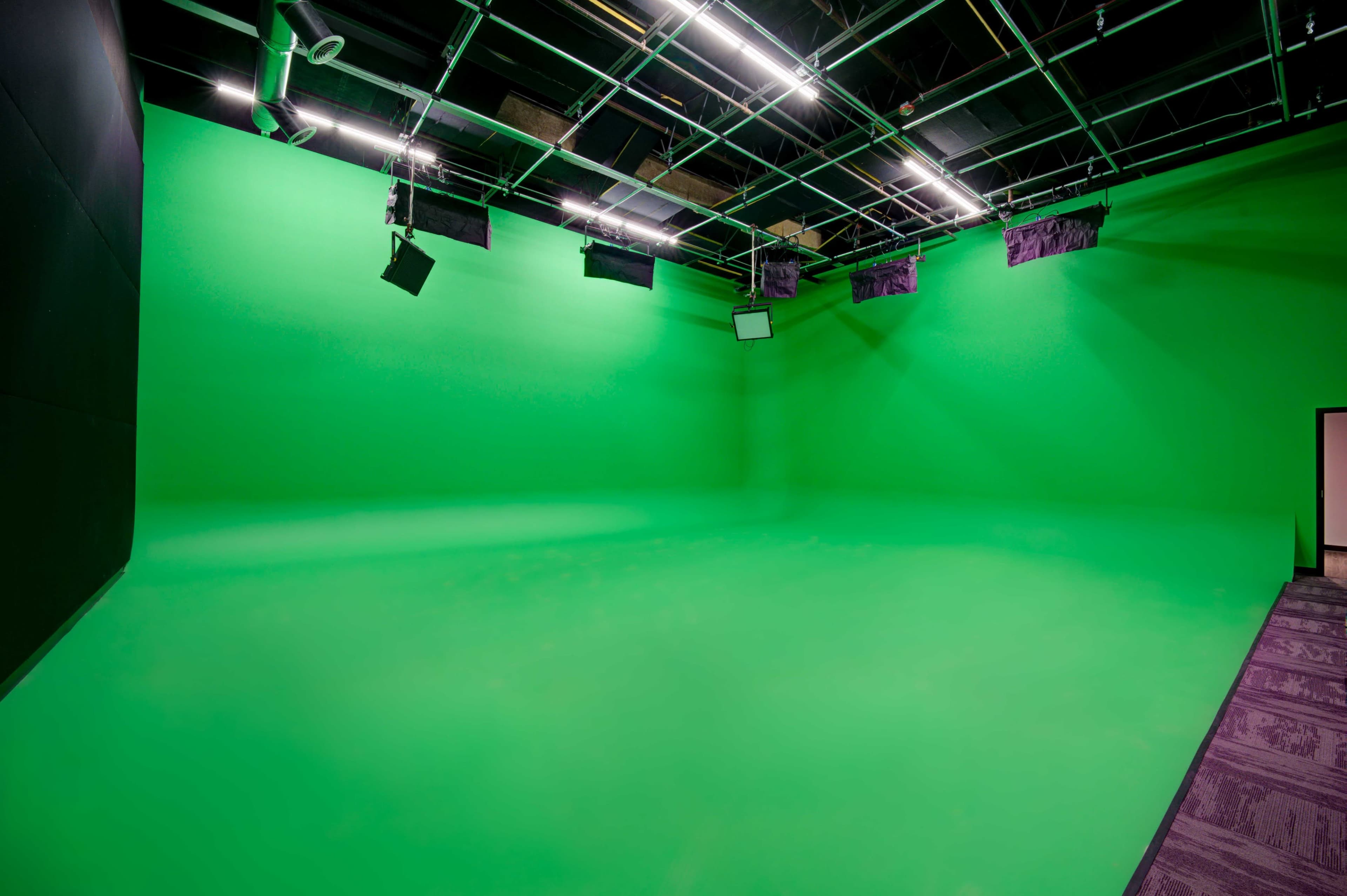 A large green screen studio with overhead lighting and dim walls.