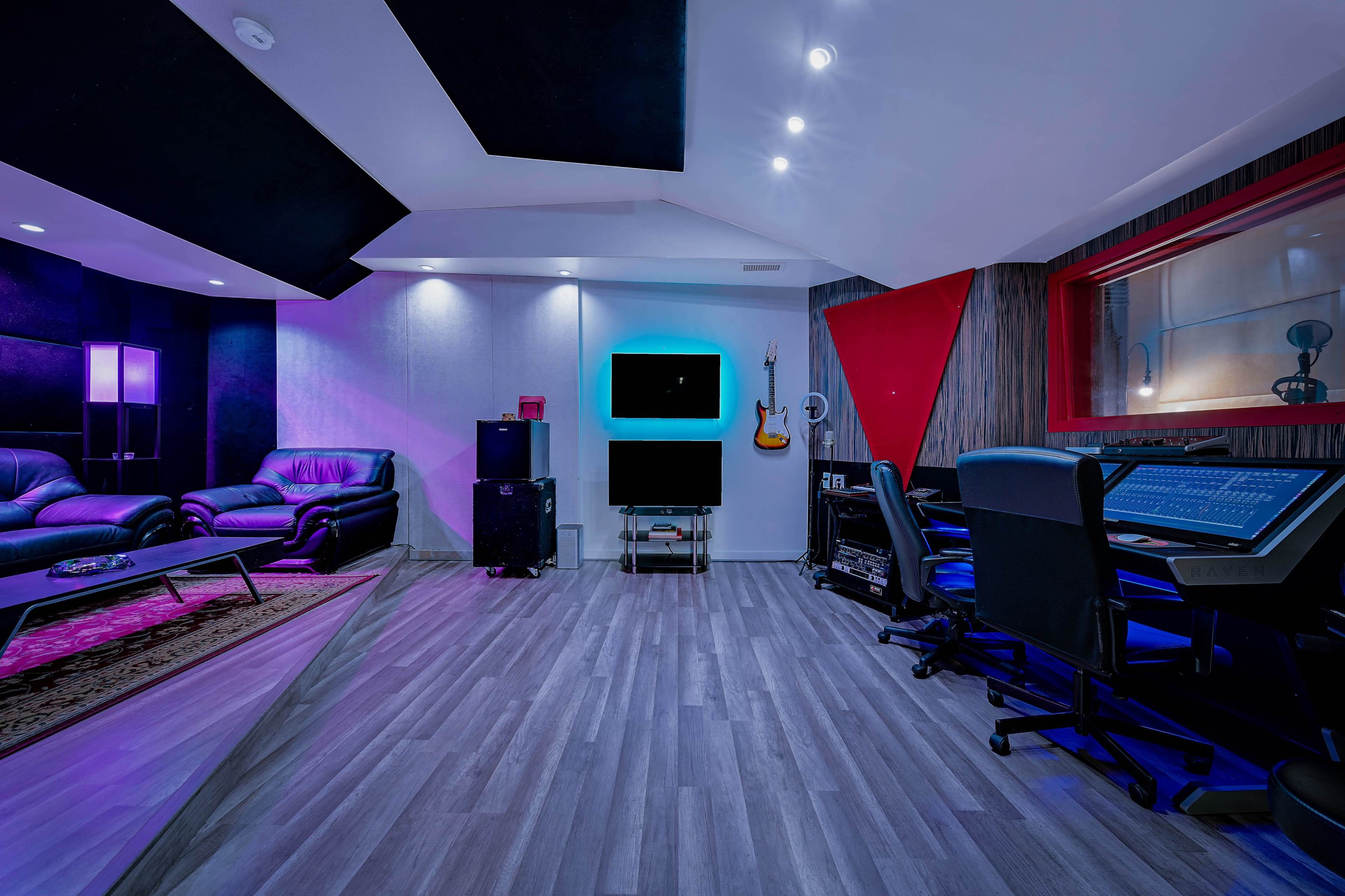 A modern recording studio featuring a comfortable seating area, a large mixing console, and colorful ambient lighting.