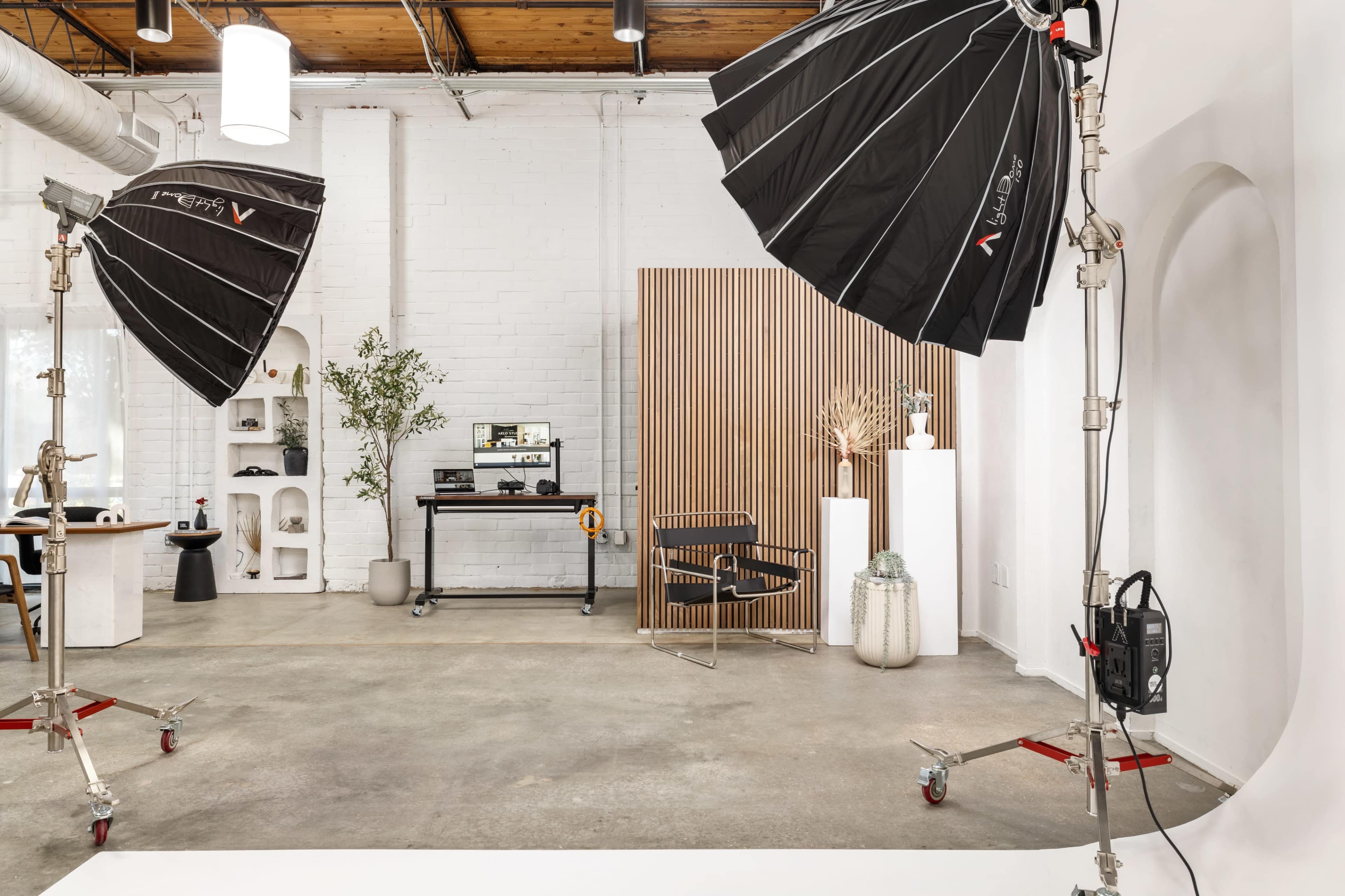 A well-lit studio space equipped with lighting equipment, a wooden backdrop, and various props arranged against a white wall.