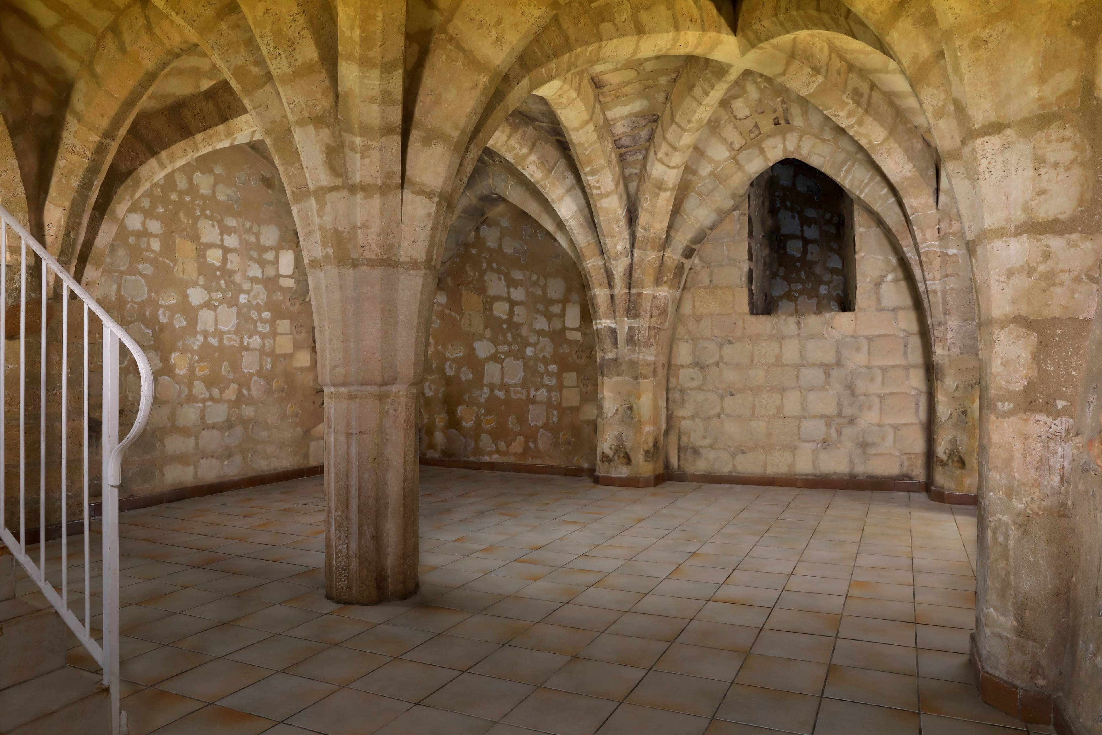 The image shows a stone-walled room with vaulted ceilings supported by arched columns and a tiled floor.