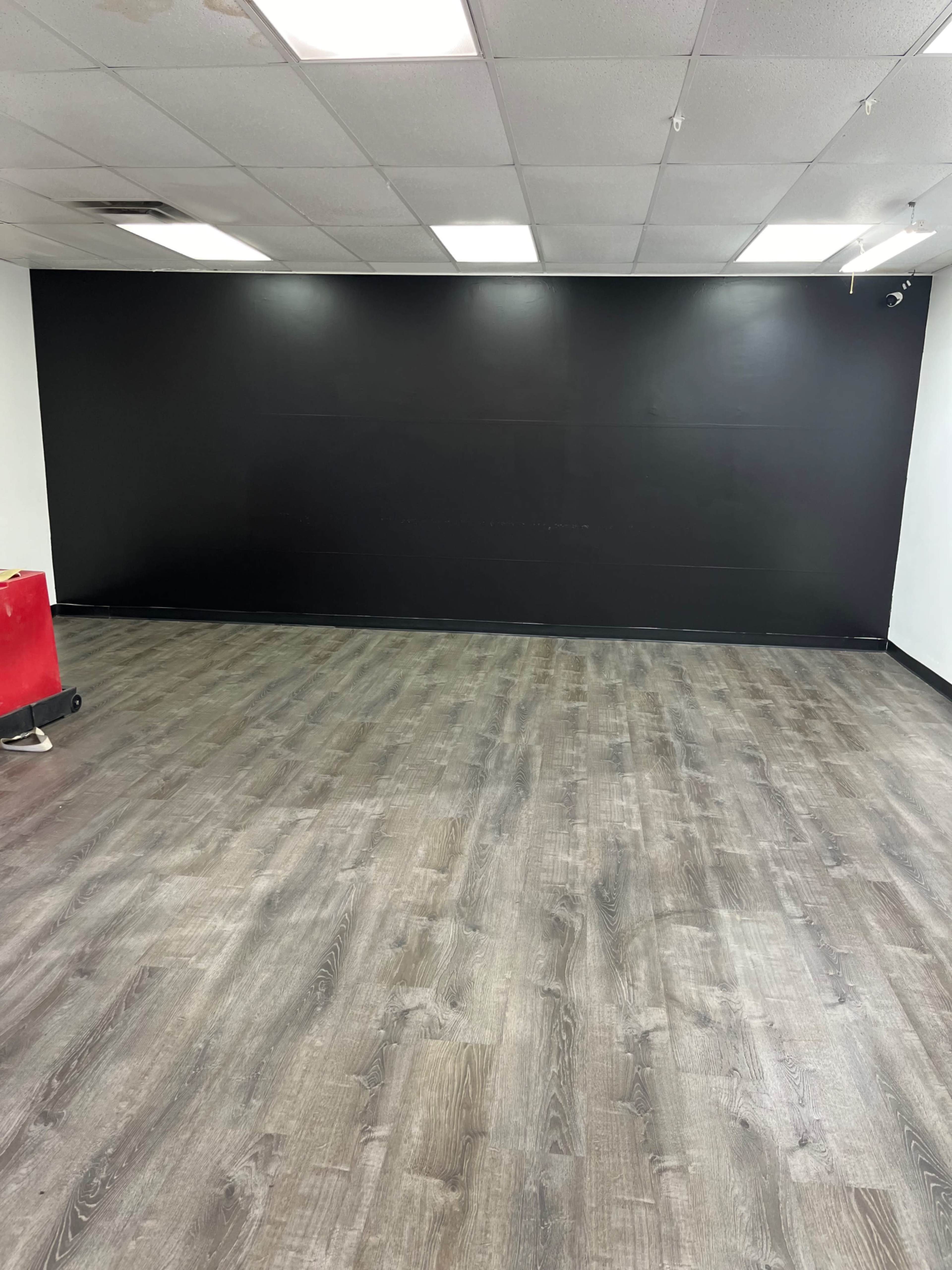 The image shows a spacious room with a black feature wall and light-colored wooden flooring.