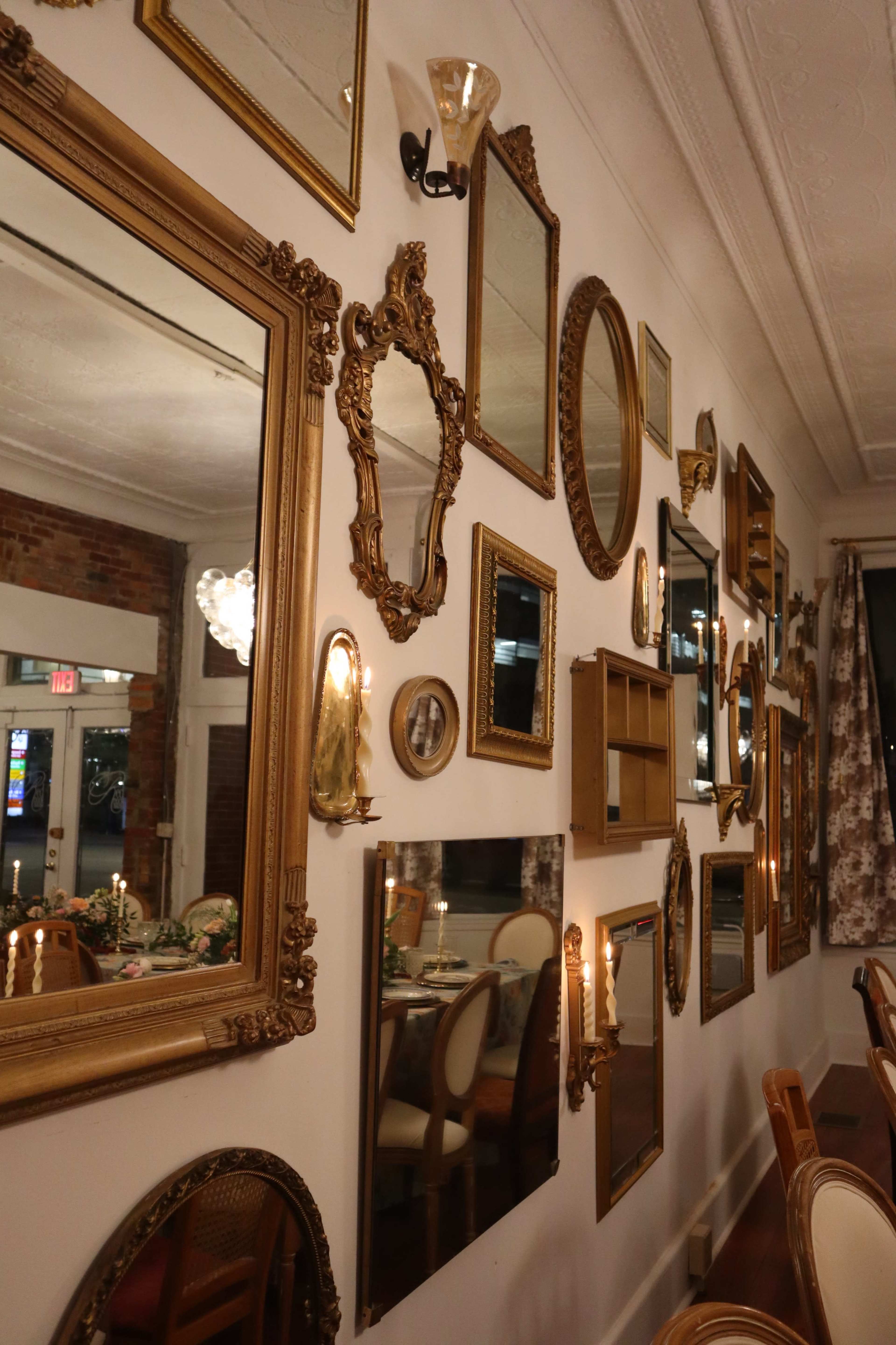 The image shows a wall decorated with various ornate mirrors and framed pieces in a dining setting.