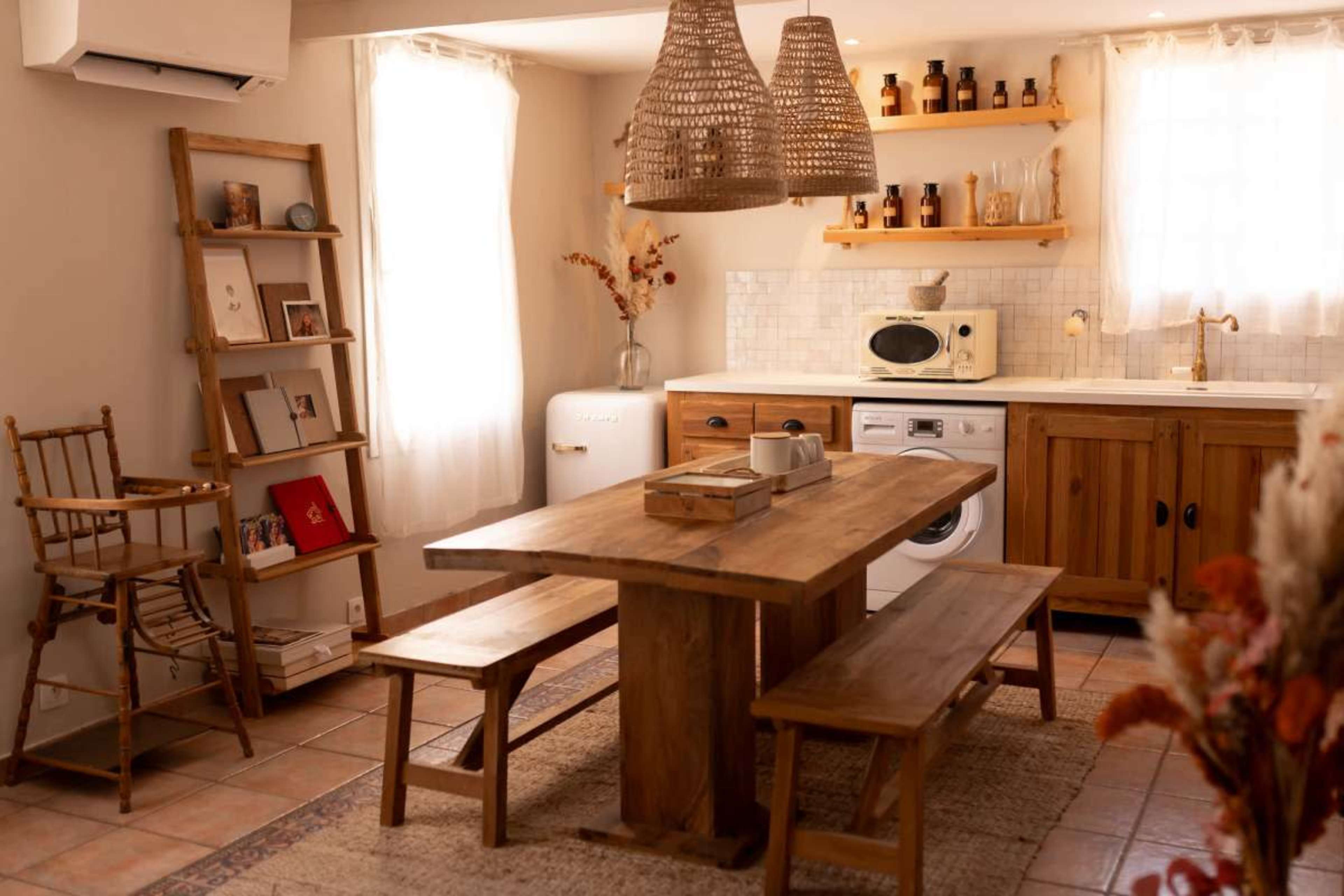 The image shows a cozy kitchen dining area with a wooden table and benches, storage shelves, and a vintage-style refrigerator.