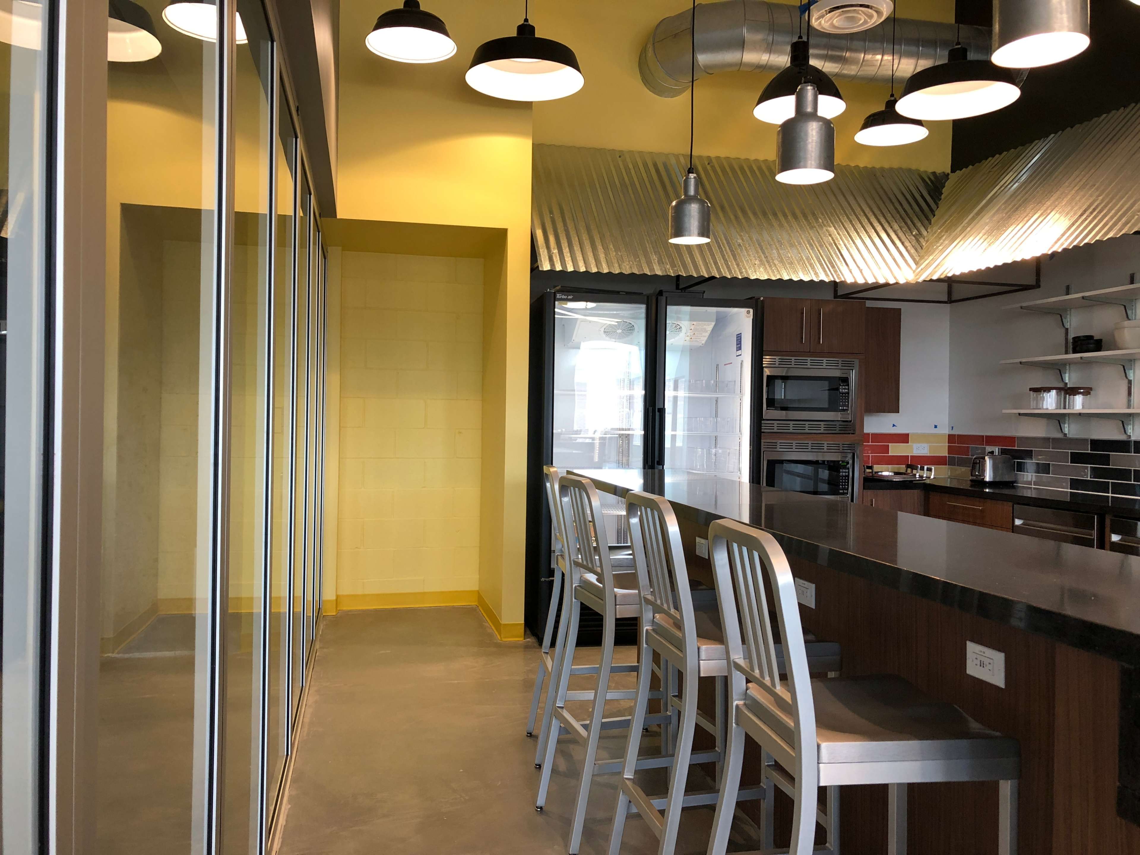 A modern kitchen with a sleek bar area featuring high stools, large glass doors, and metallic accents on the ceiling.