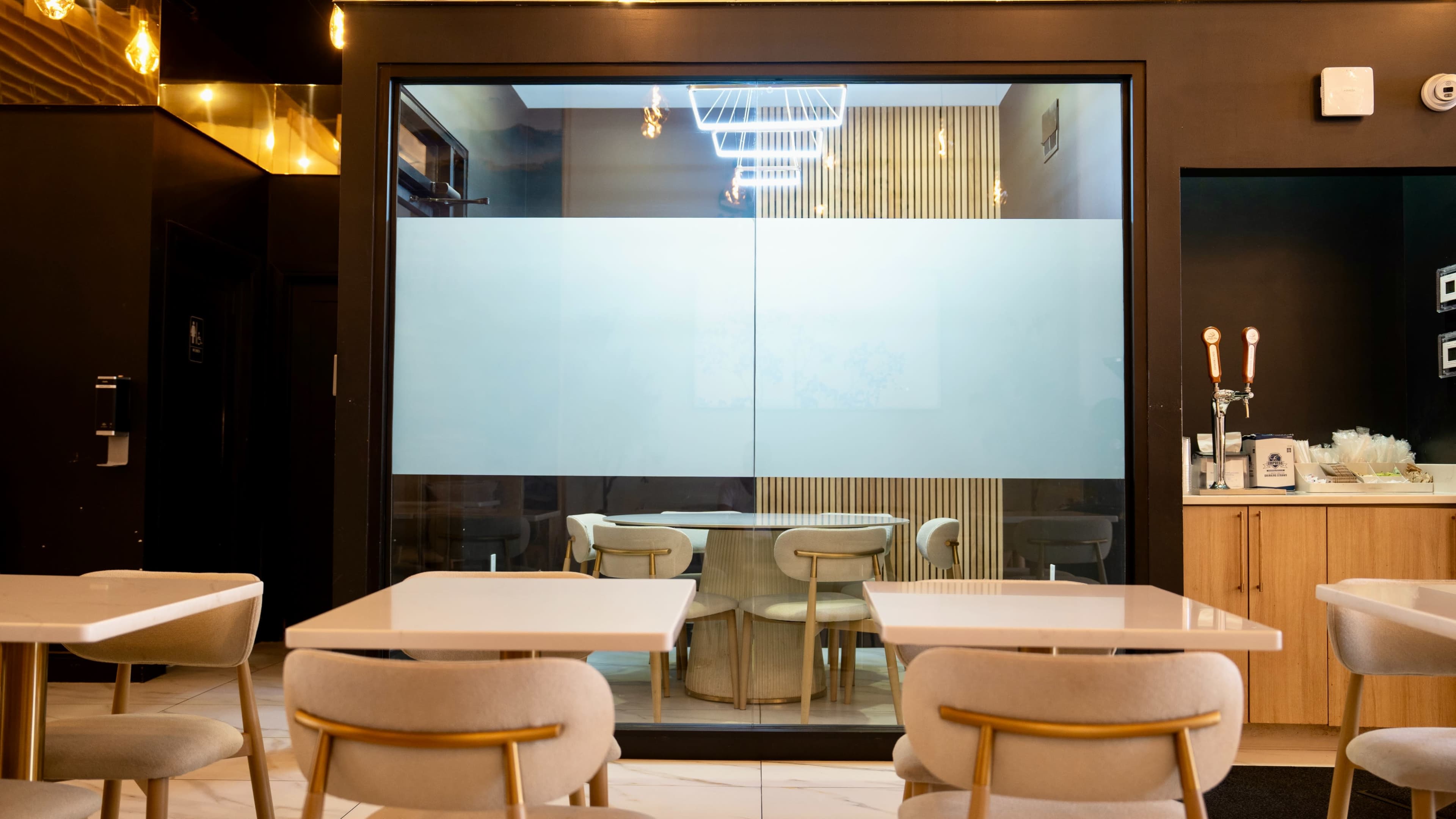A modern café interior features a glass-walled private dining area with seamless tables and chairs.
