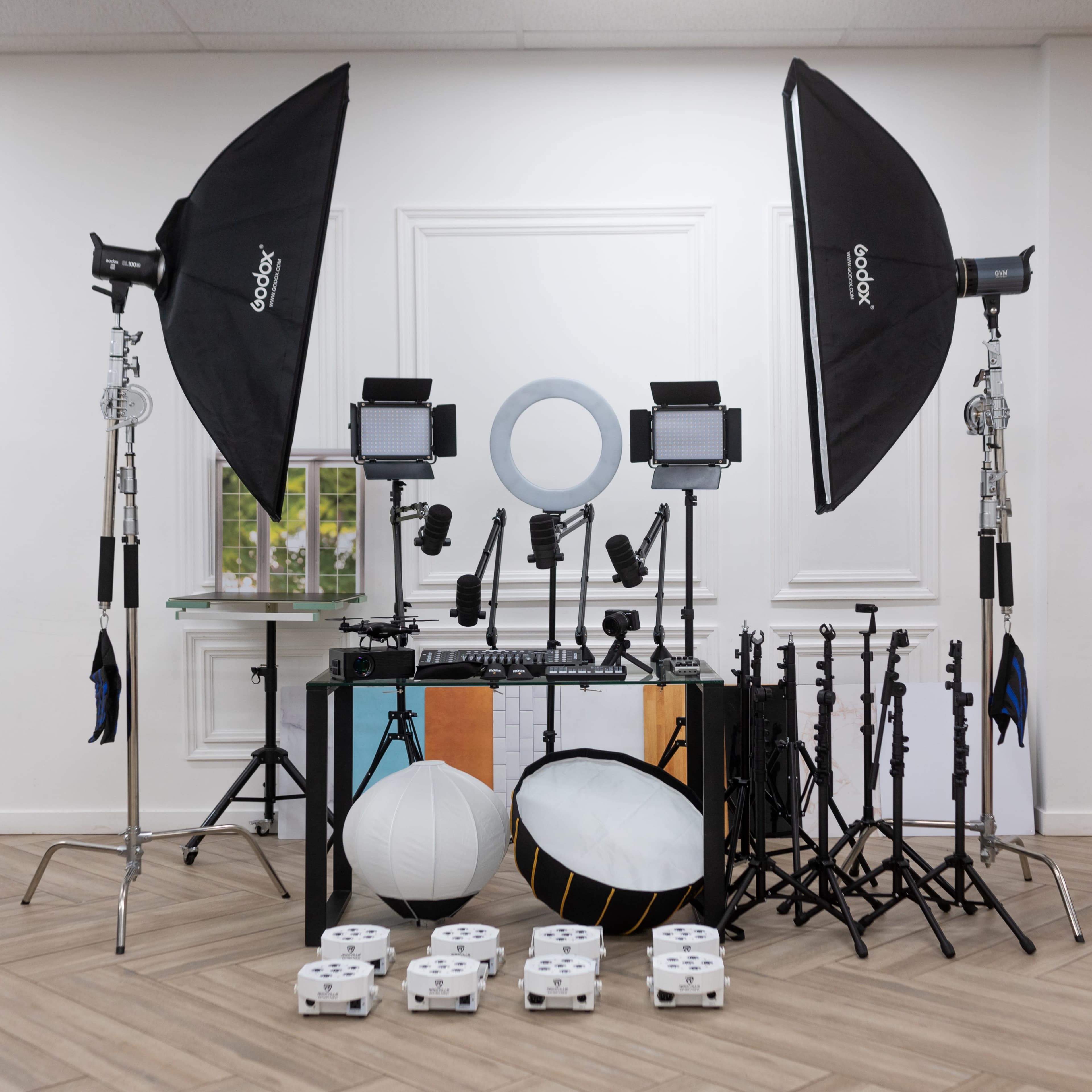 The image shows a photography setup featuring multiple light stands, softboxes, and various lighting equipment arranged in a studio space.