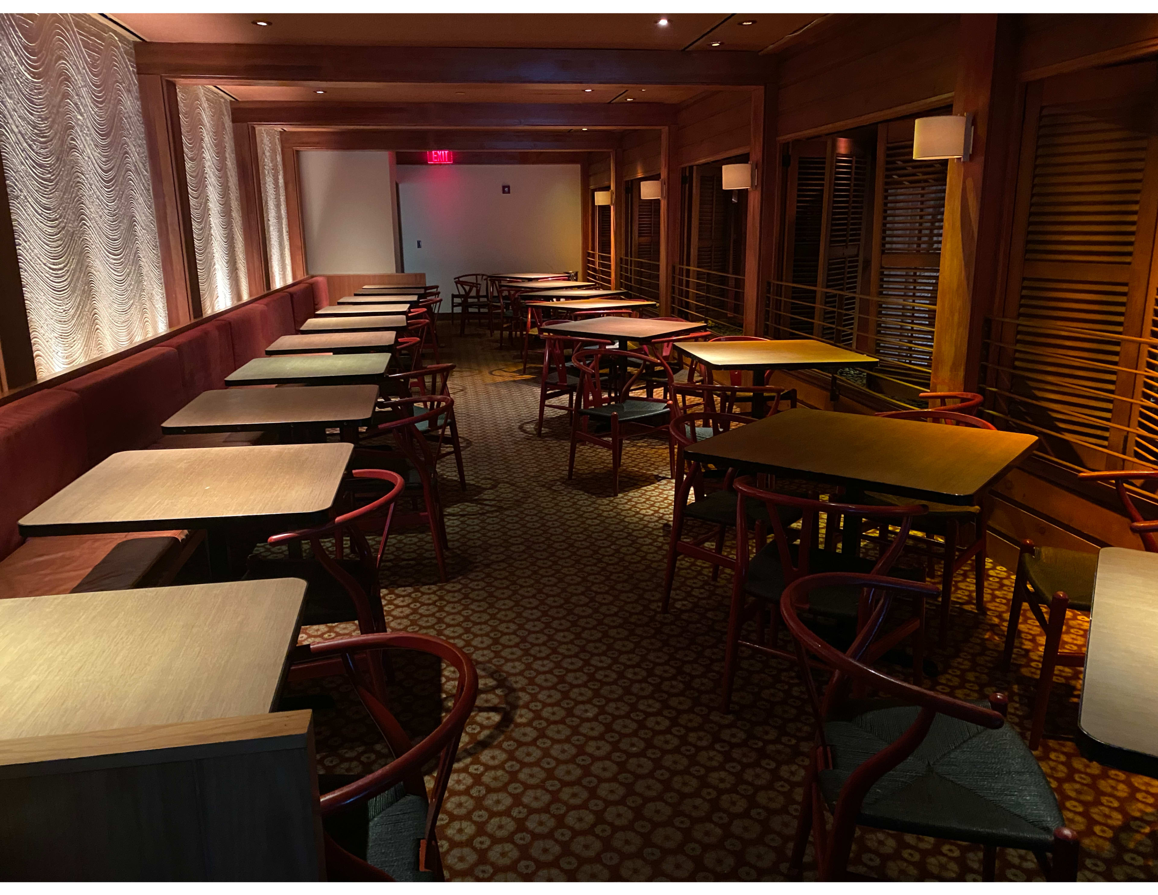 A dimly lit interior of a restaurant or café with empty tables and wooden seating arranged in rows.