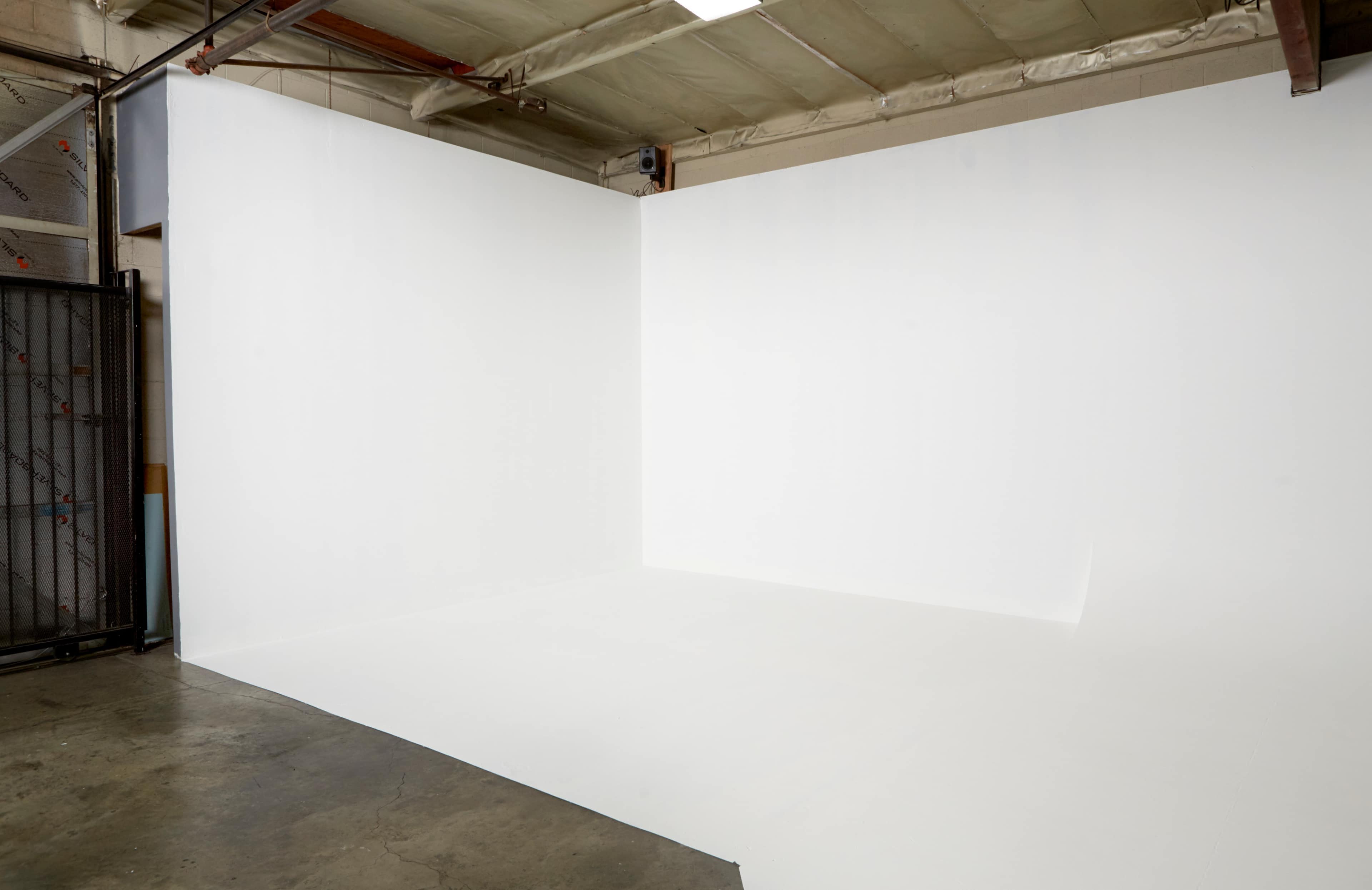 A spacious, minimalistic studio with a white backdrop and smooth concrete flooring.