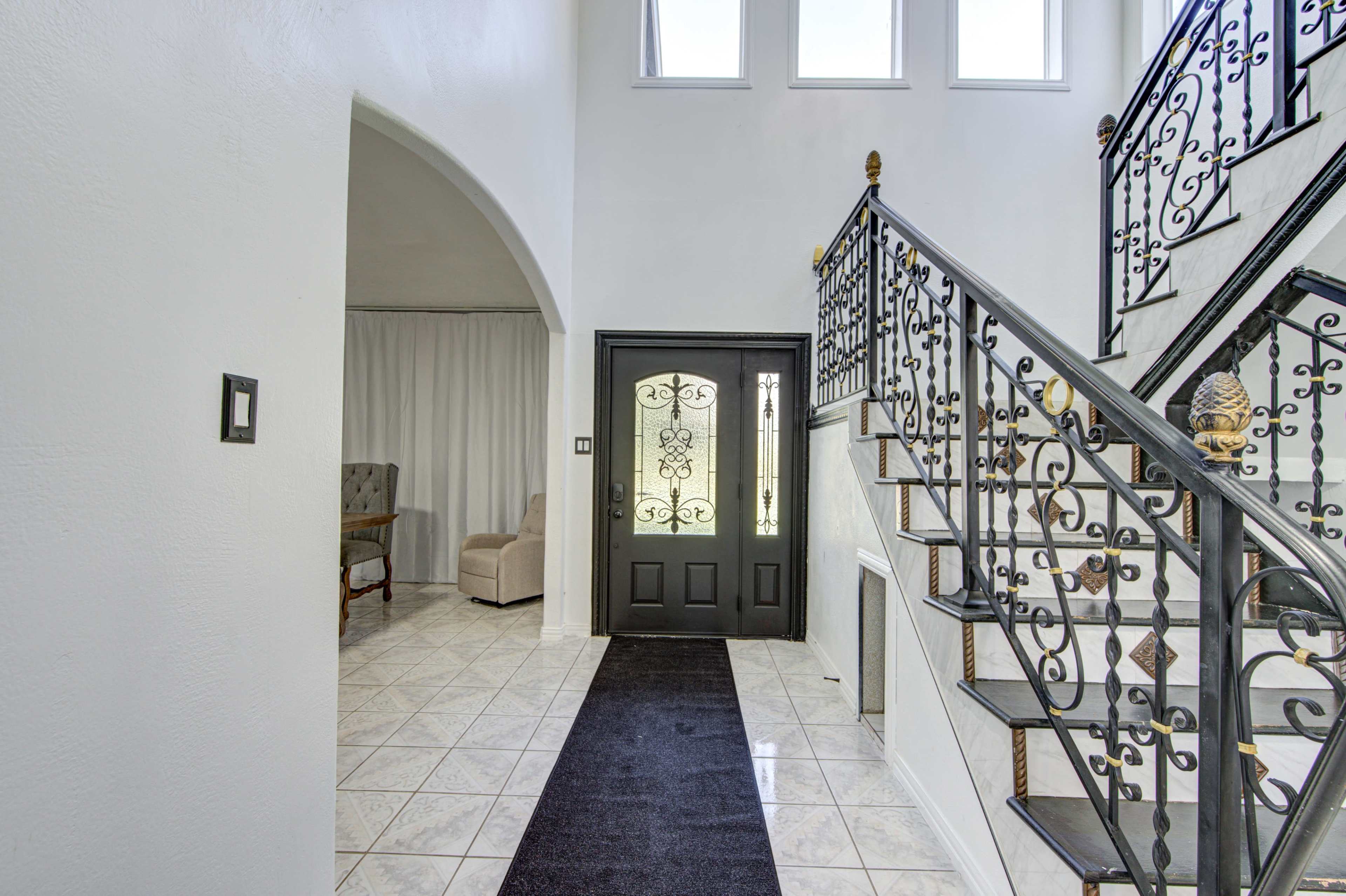 A spacious entryway featuring a black wrought iron staircase, a decorative front door, and tiled flooring.