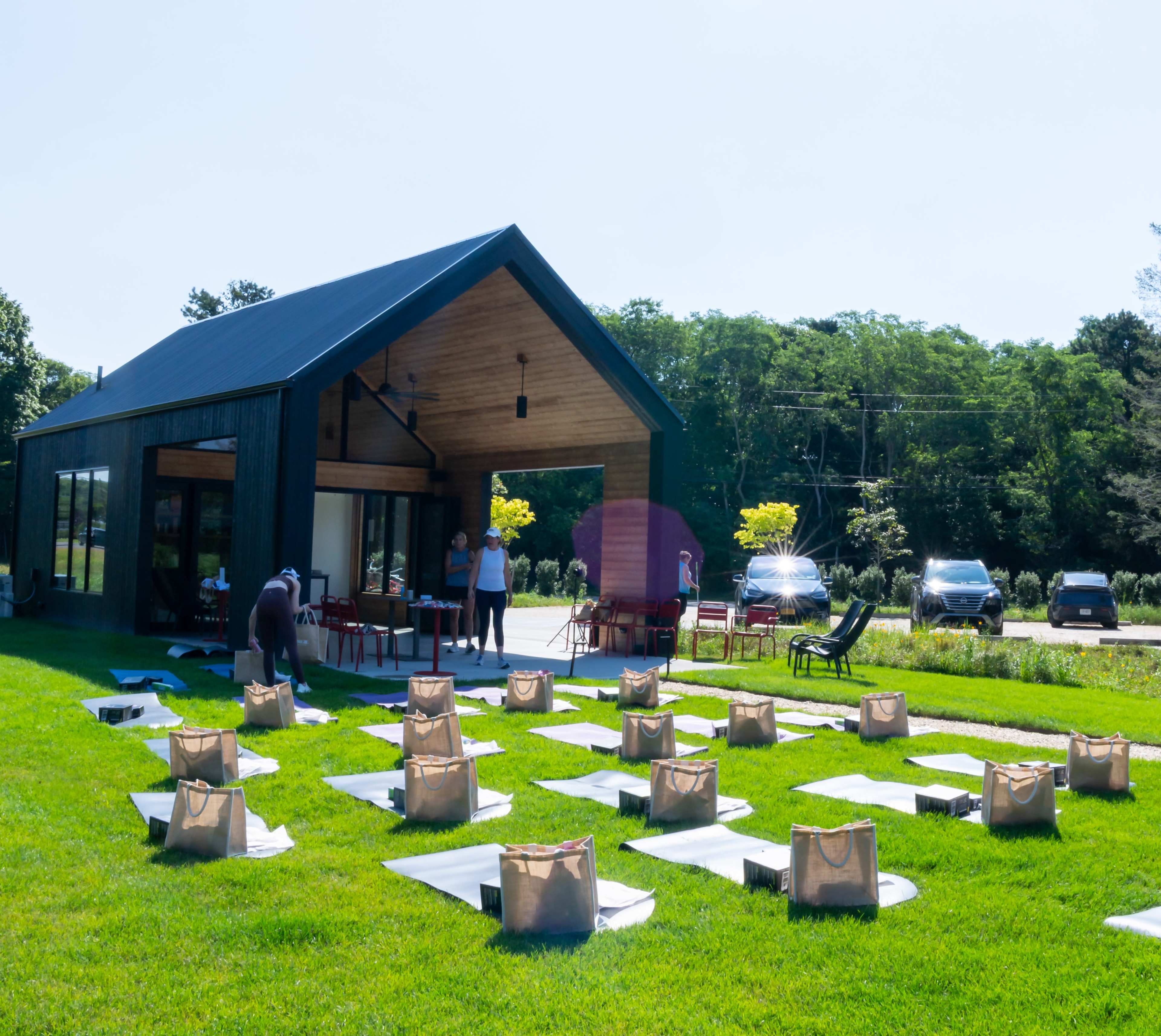 A modern building sits in a grassy area, with yoga mats placed in rows outside and two people preparing in front of it.