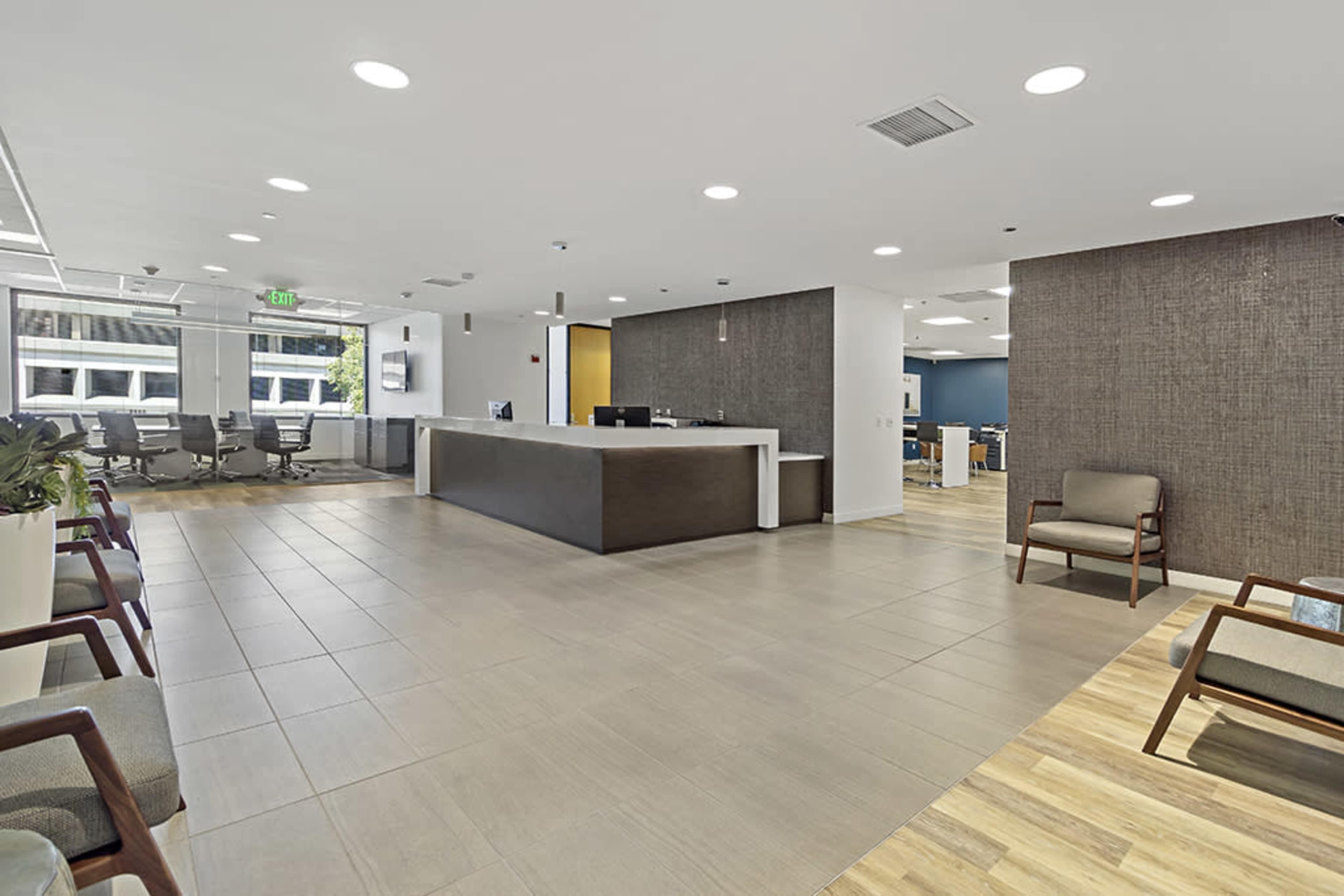 The image shows a modern office reception area with a front desk and seating for visitors, surrounded by an open workspace.