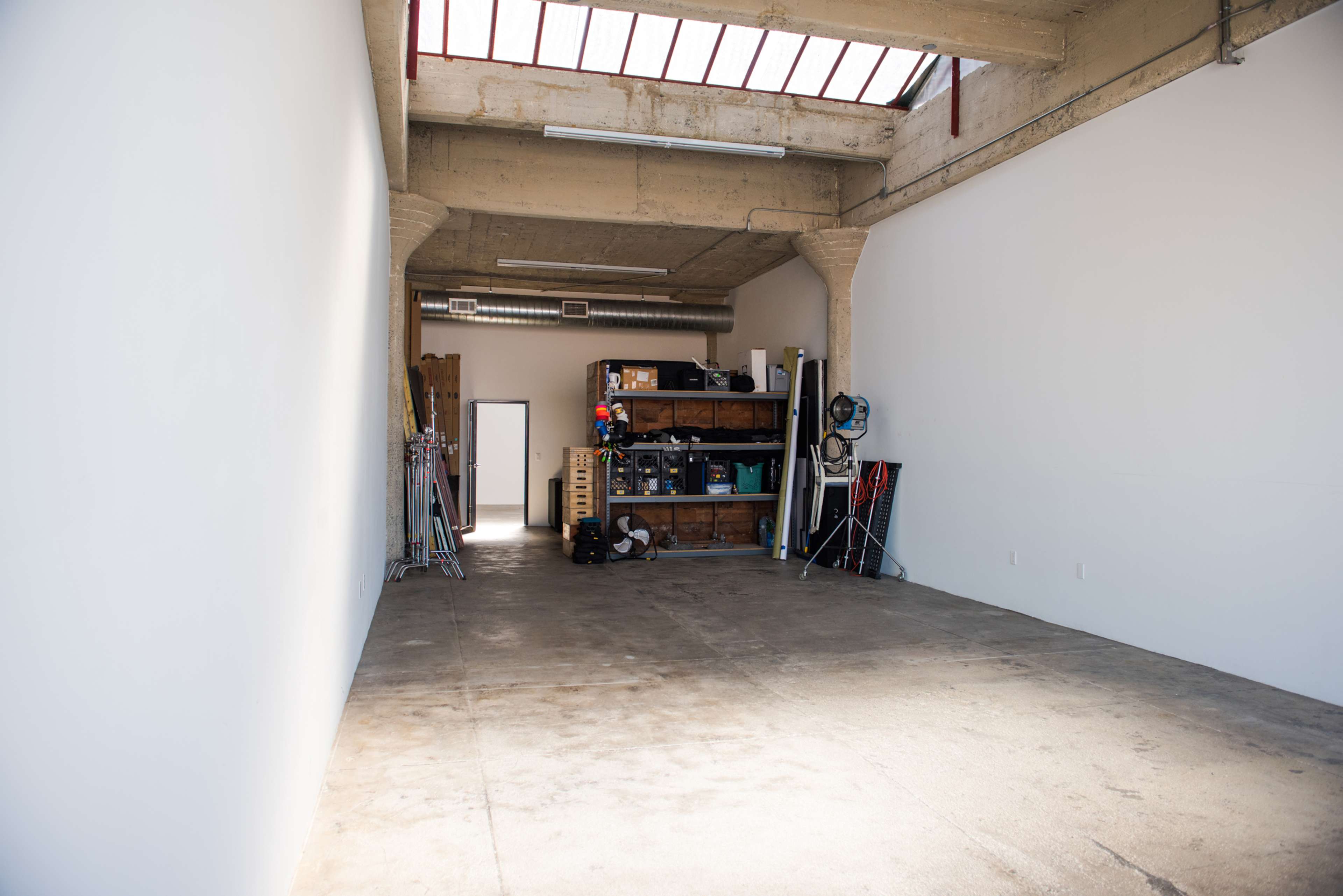 An empty room with concrete flooring and a storage unit filled with various equipment along one wall.