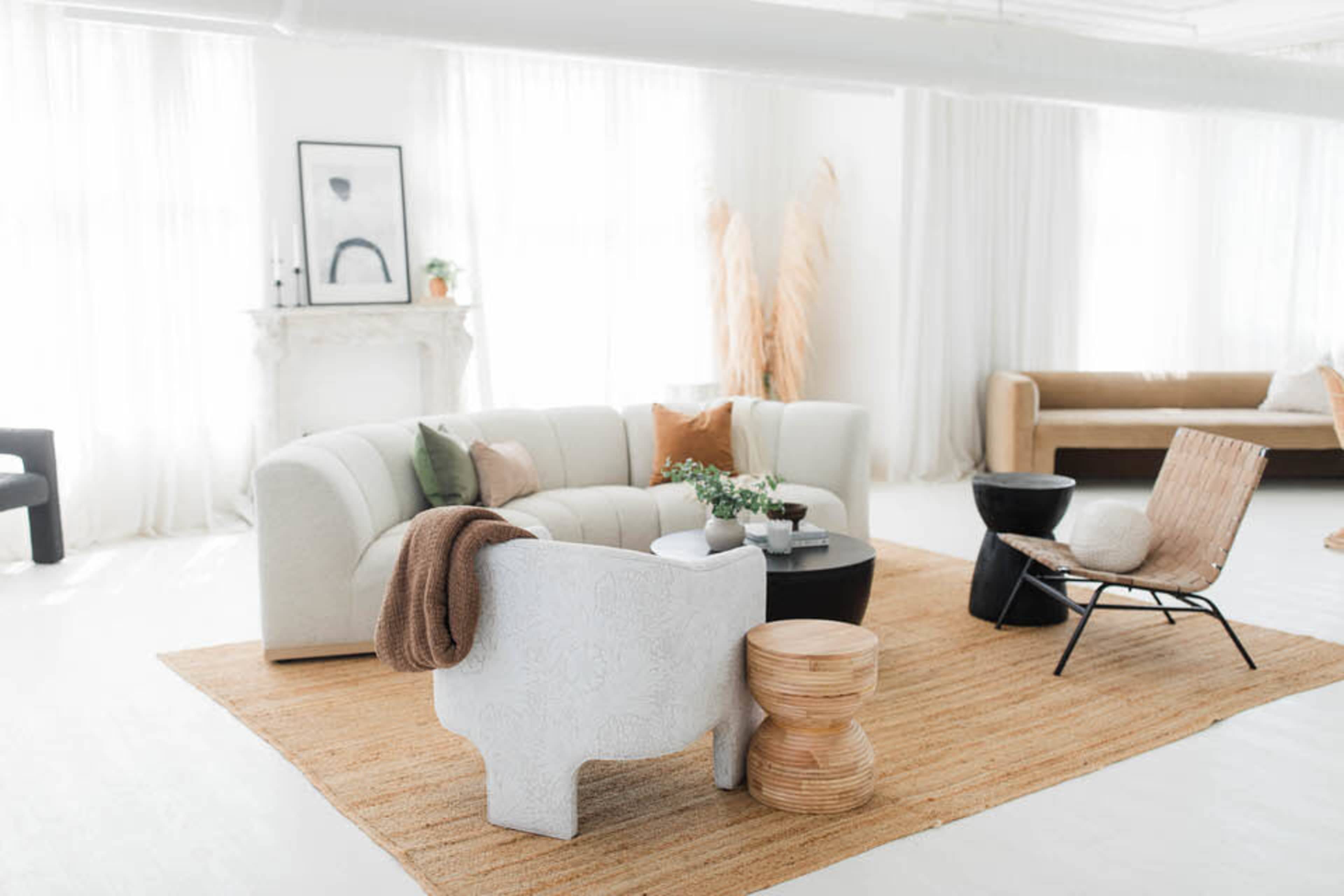 The image shows a modern living room with a curved sofa, a round coffee table, and various seating arrangements, all set on a textured area rug.