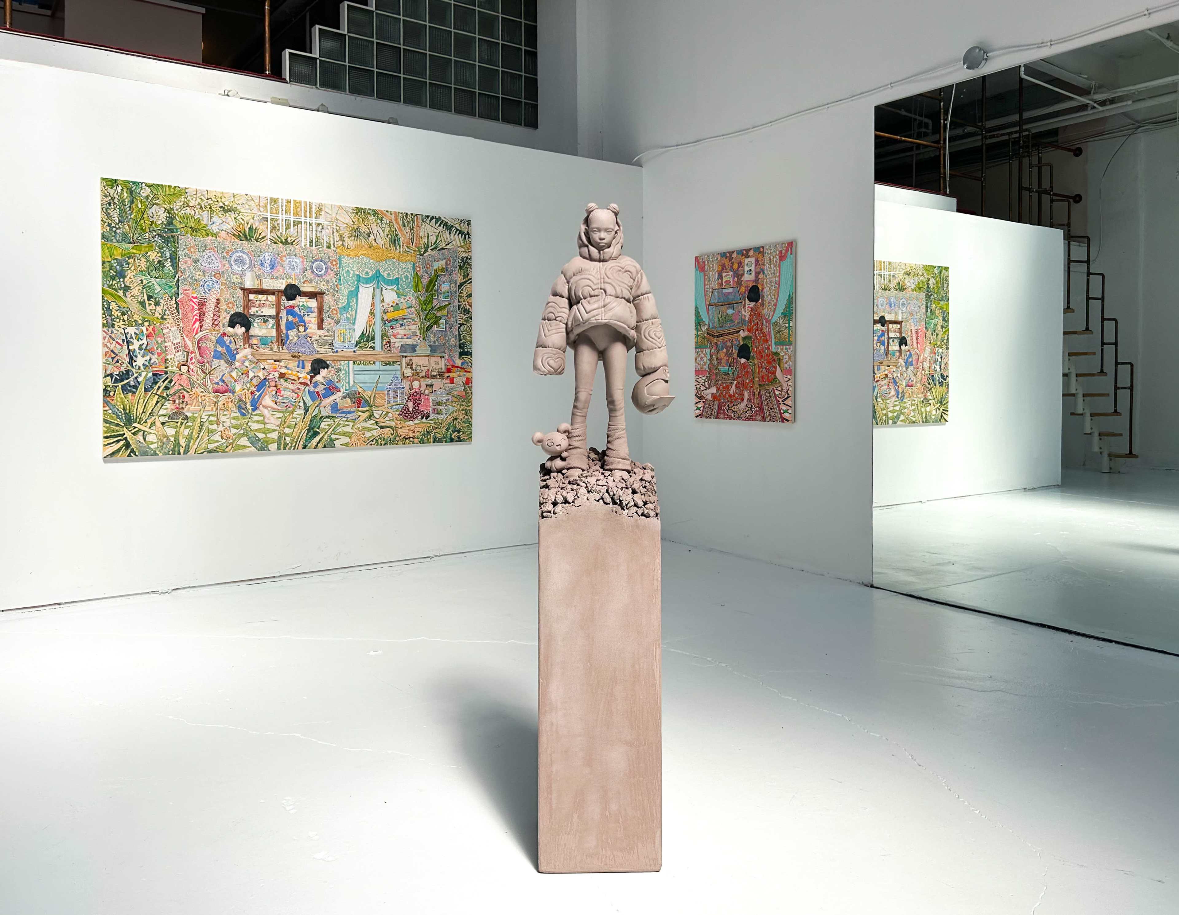 The image shows an art gallery with a central sculpture on a pedestal, surrounded by colorful wall paintings in a bright, open space.