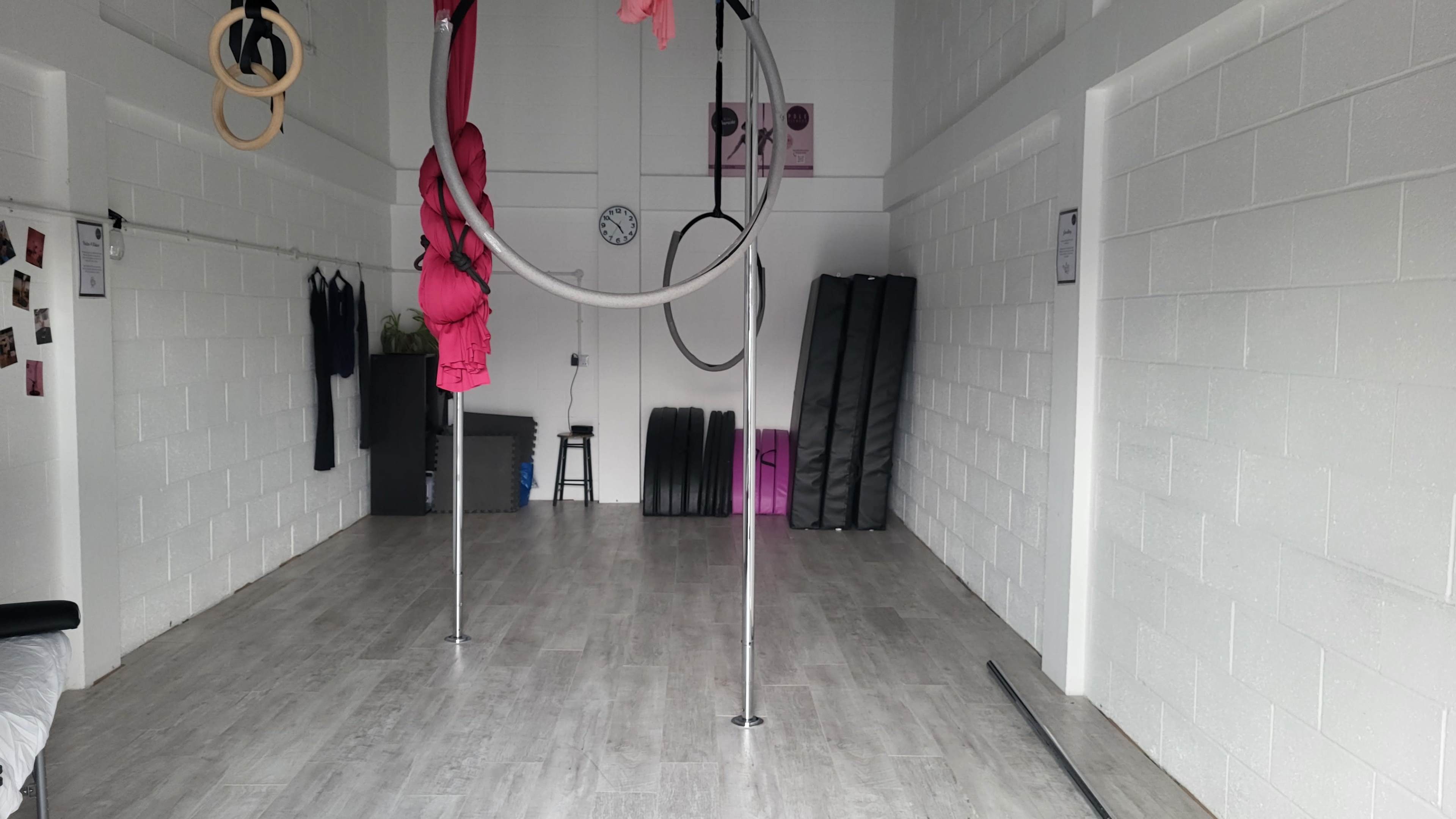 The image shows a spacious indoor gym area with aerial equipment, including hoops and silk fabric, and minimal furnishings against a white wall.